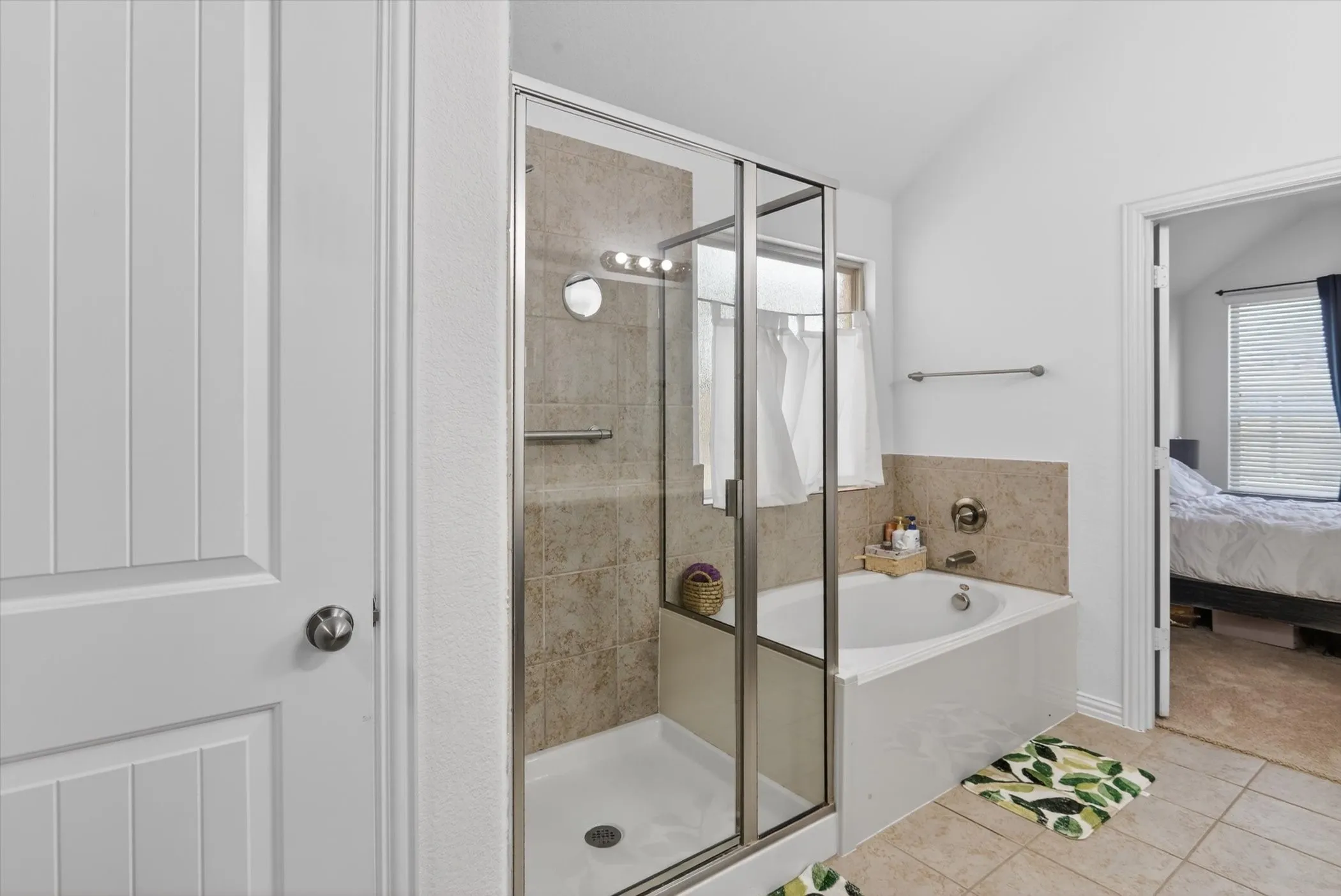 Shower with glass enclosure, white soaking tub, and neutral tiled flooring