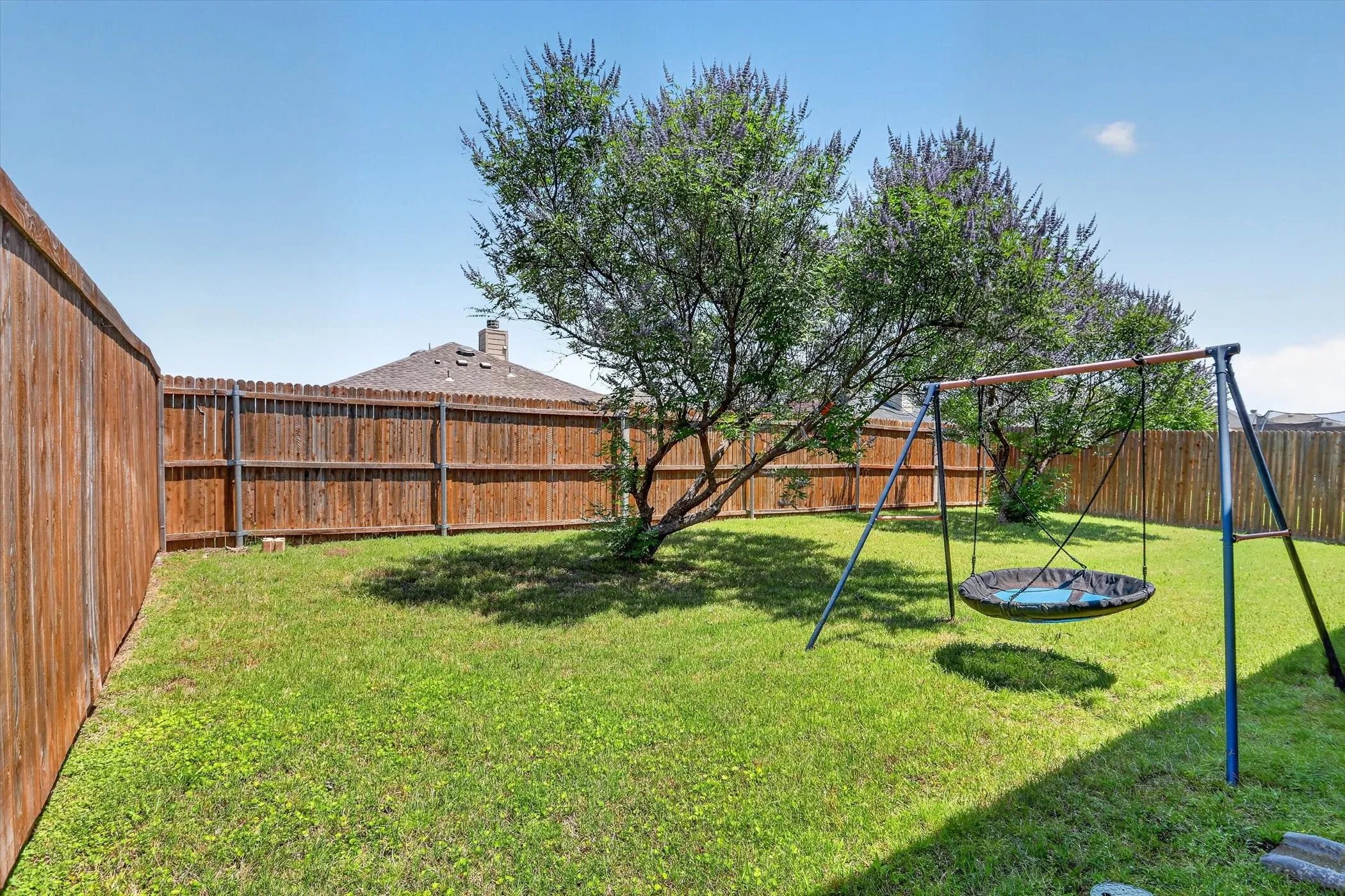 Expansive backyard featuring a manicured lawn, established trees, and perimeter wood fencing