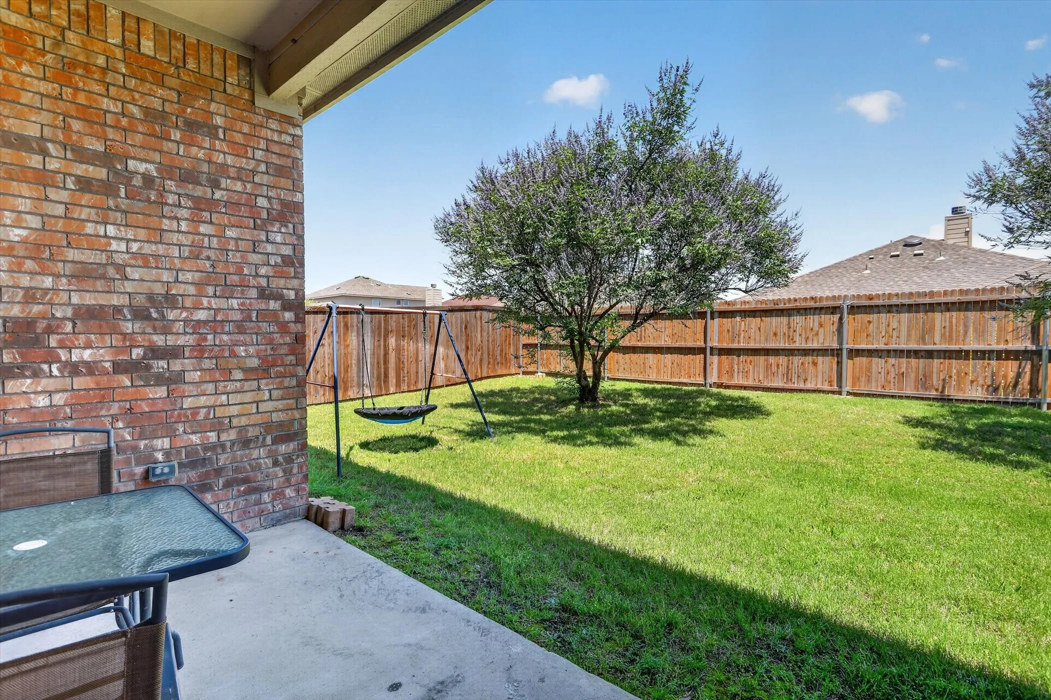 Expansive backyard featuring a privacy fence, mature trees, and a spacious concrete patio