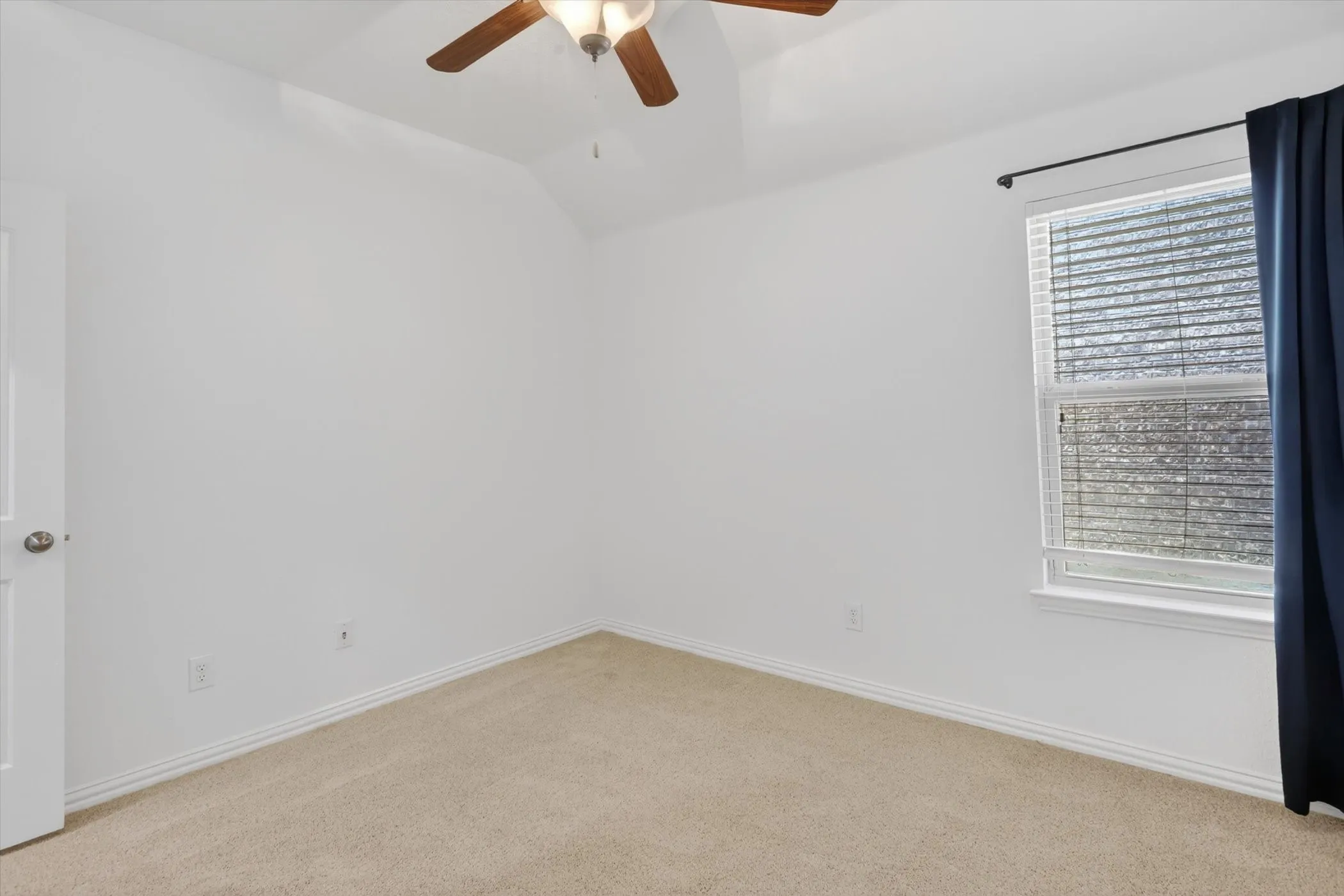 Room featuring light beige carpeting, white walls, and a vaulted ceiling with a wood-finish ceiling fan and light fixture