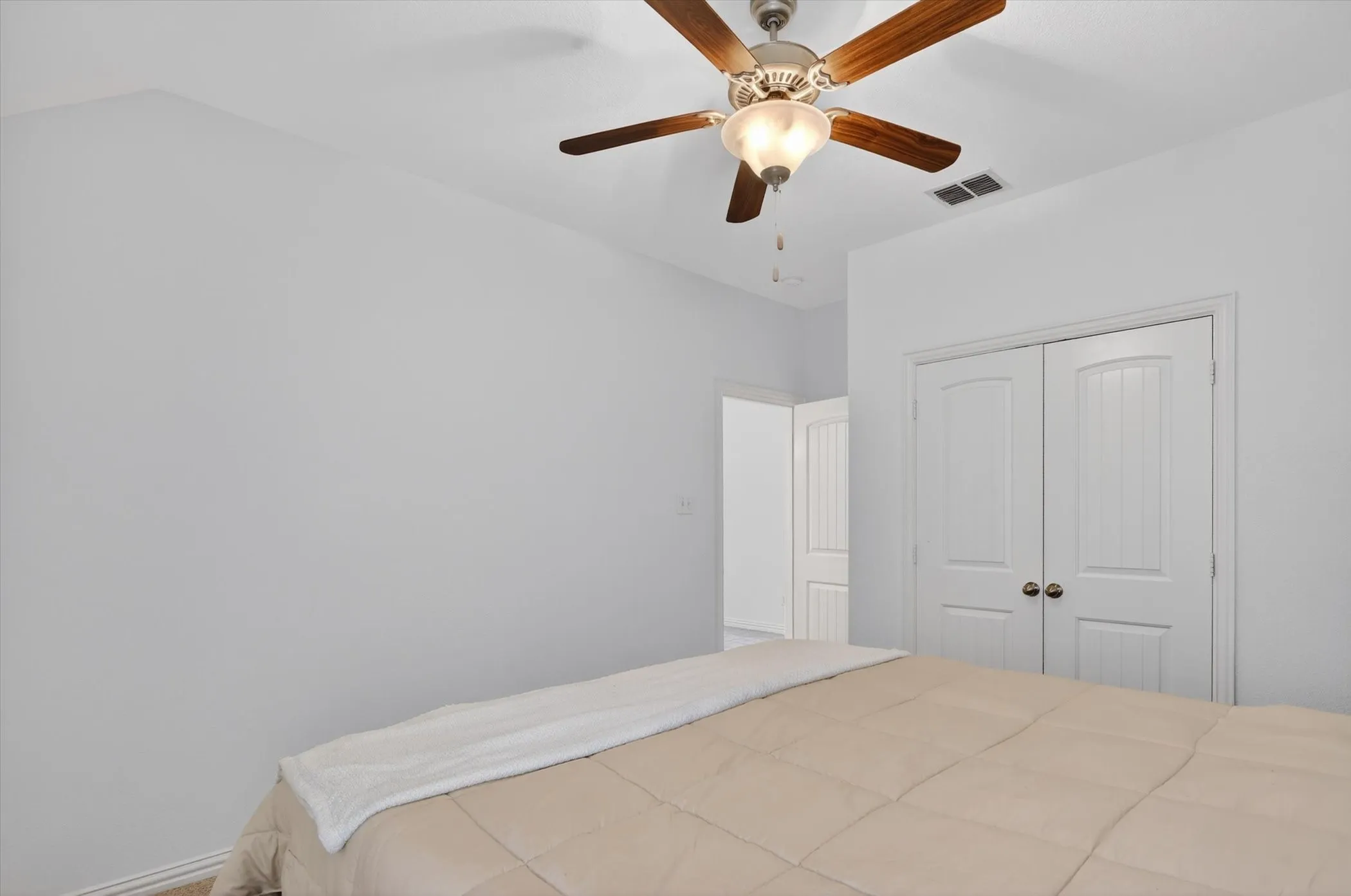 Room featuring a ceiling fan with wood-finish blades, white walls, and a light-colored ceiling