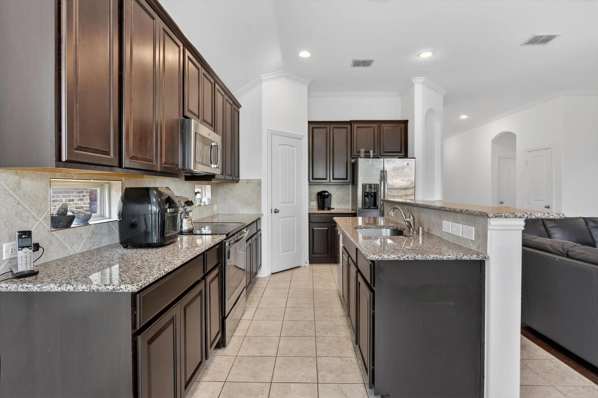 Kitchen featuring dark wood cabinetry, light granite countertops, stainless steel appliances, tile flooring, and recessed lighting