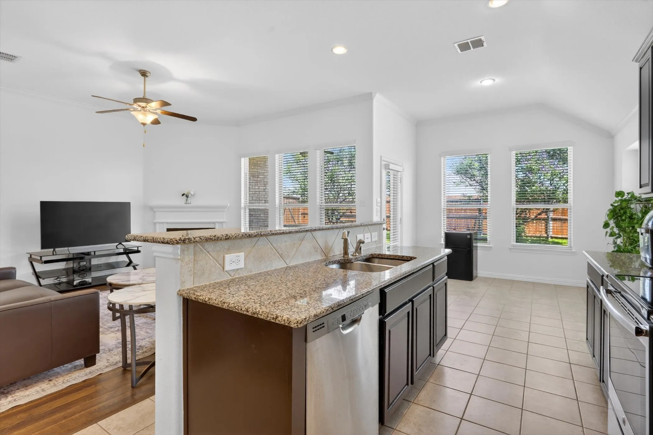 Kitchen island featuring granite countertops, a stainless steel double basin sink, and integrated stainless steel dishwasher
