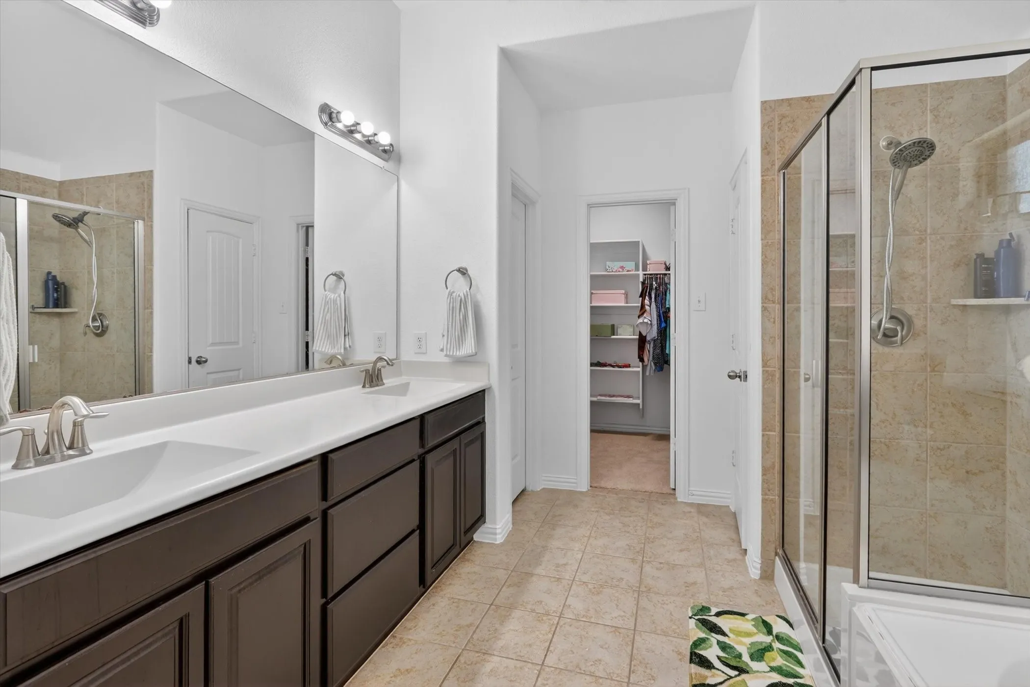 Spacious bathroom featuring a dual vanity with dark wood cabinetry, a large mirrored wall, and brushed nickel fixtures