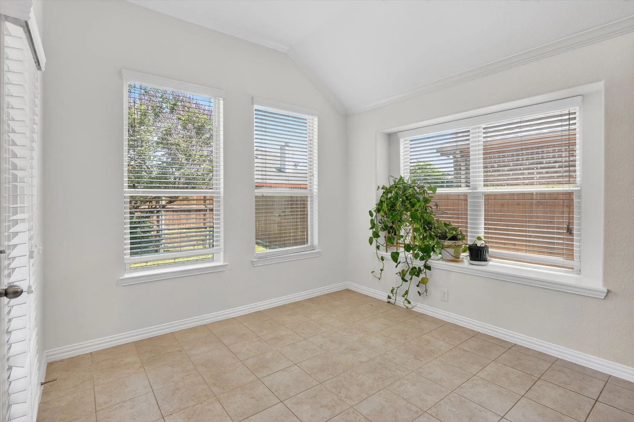 Bright room featuring multiple windows, a vaulted ceiling, and neutral-toned tile flooring
