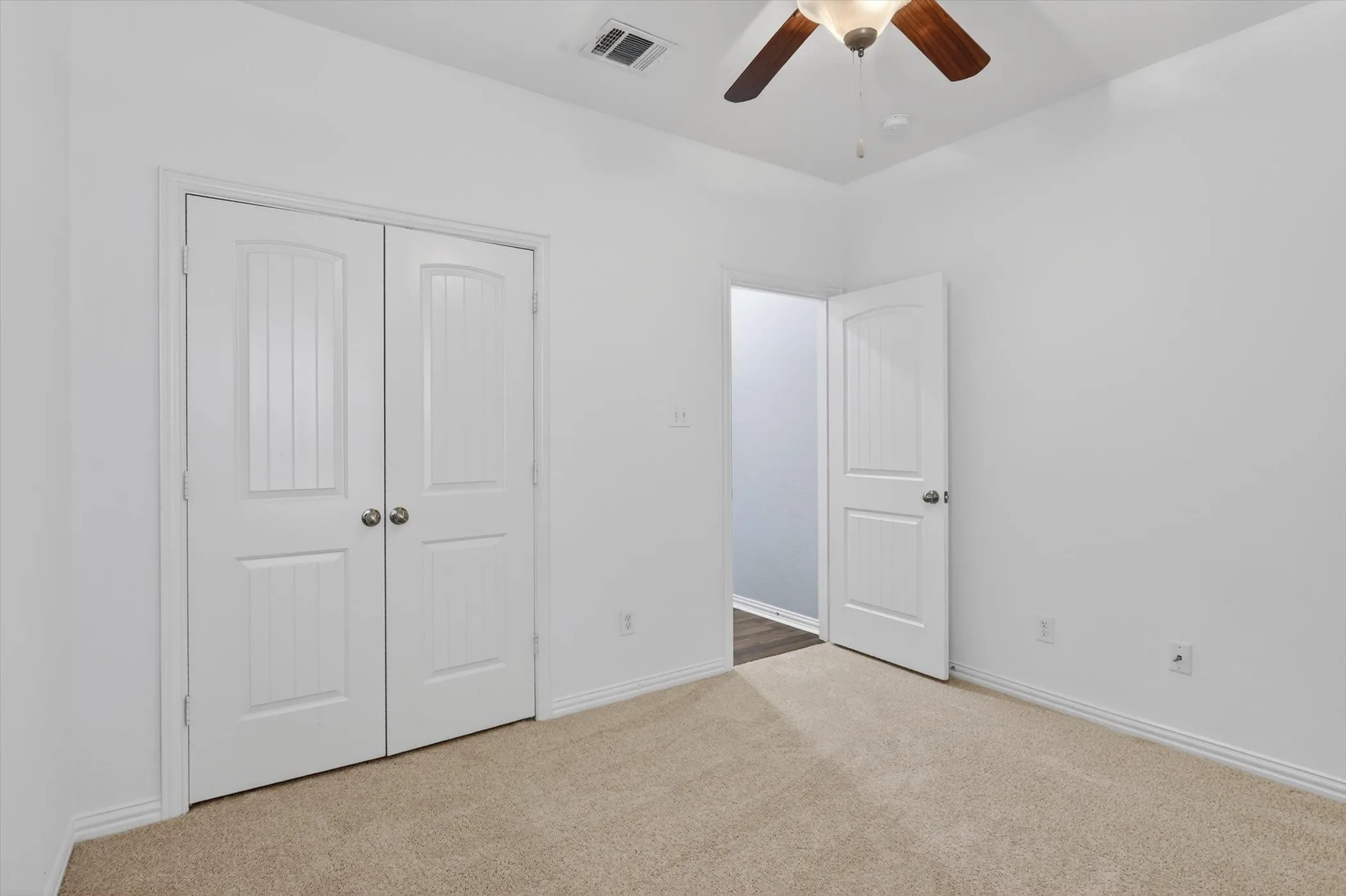 Room featuring neutral carpet flooring, white walls, and a ceiling fan with wood-finish blades