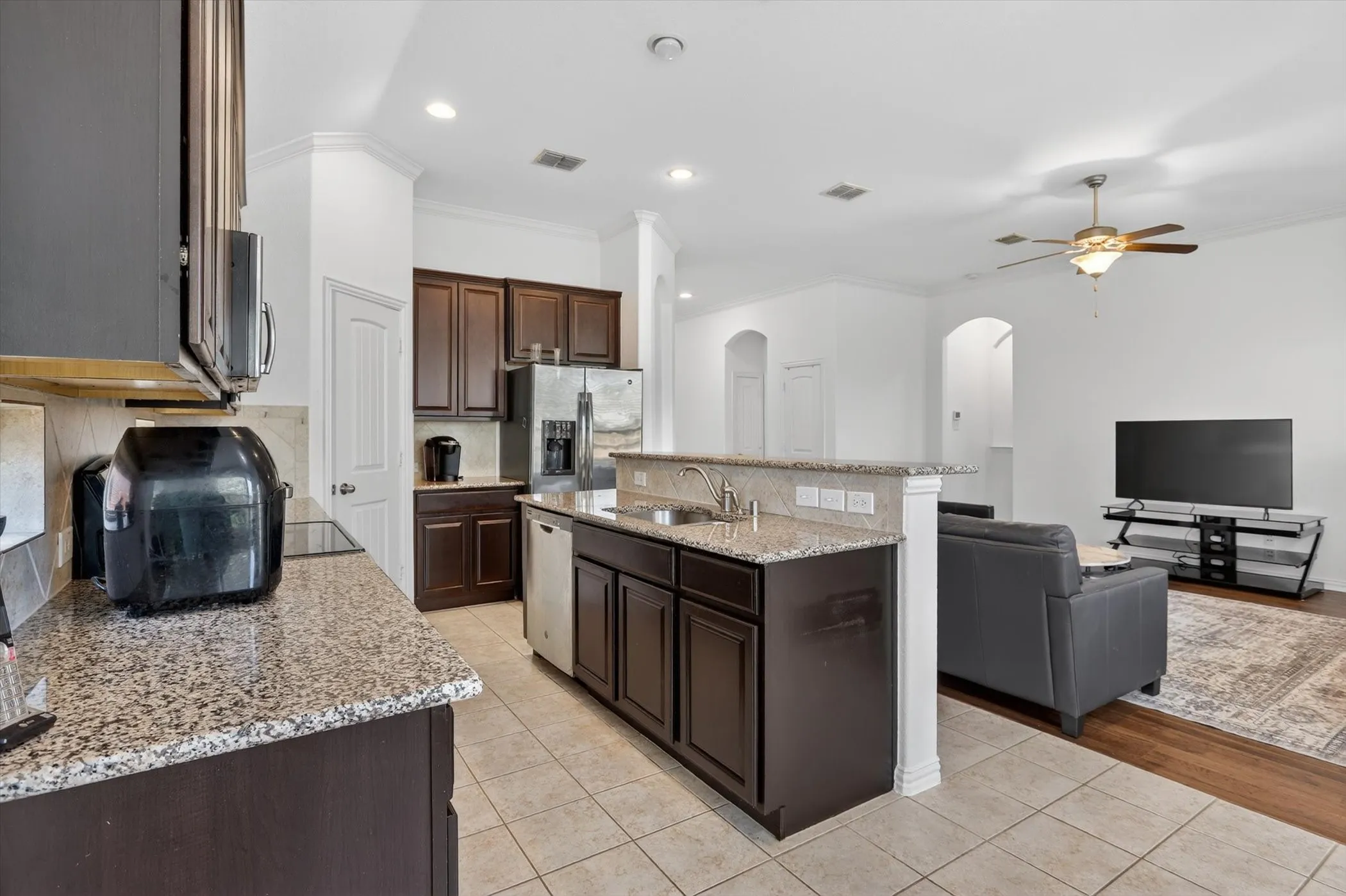 Open-concept kitchen and living area featuring granite countertops, dark wood cabinetry, a built-in stainless steel dishwasher, and tile flooring