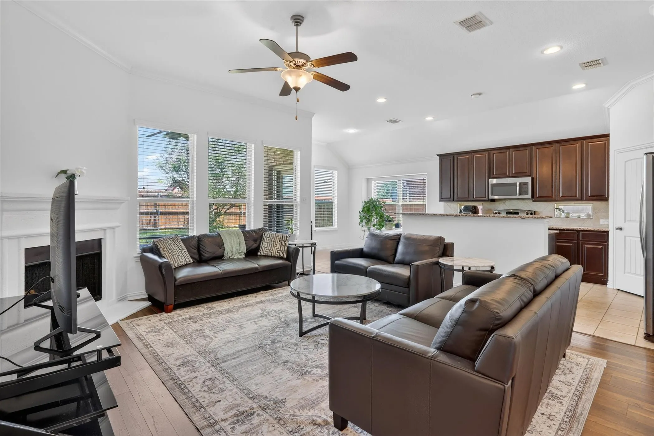 Vaulted ceiling living area featuring a fireplace with white mantel, wood-finish flooring, and multiple windows