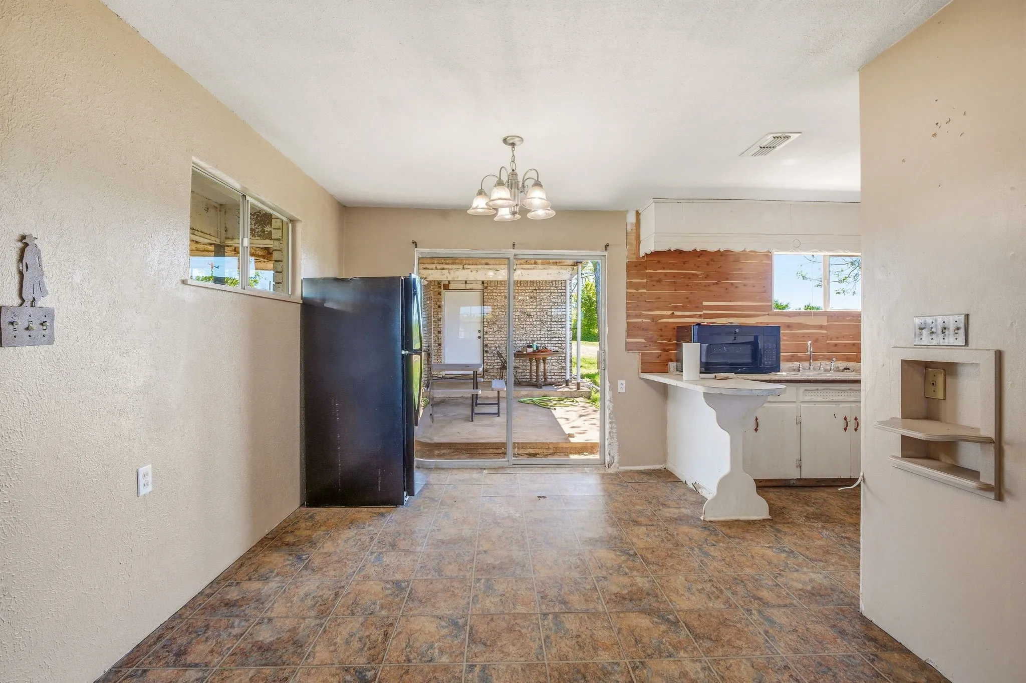Kitchen with black appliances, suspended lighting, a textured wall, light countertops, and stone finish floors