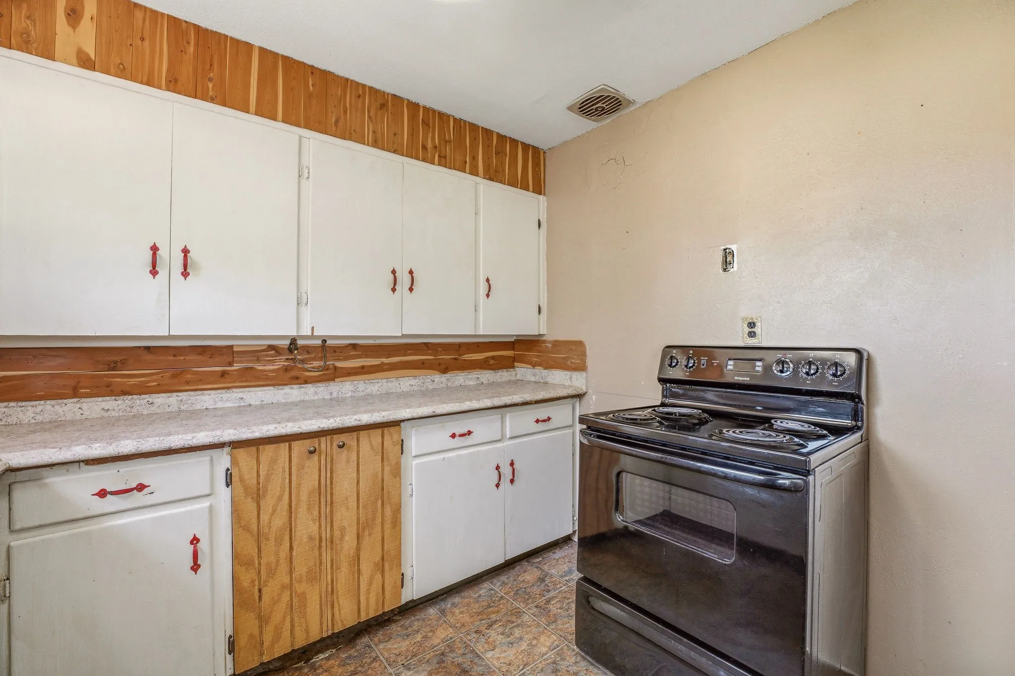 Kitchen featuring black electric range oven, light countertops, white cabinetry, and stone finish flooring
