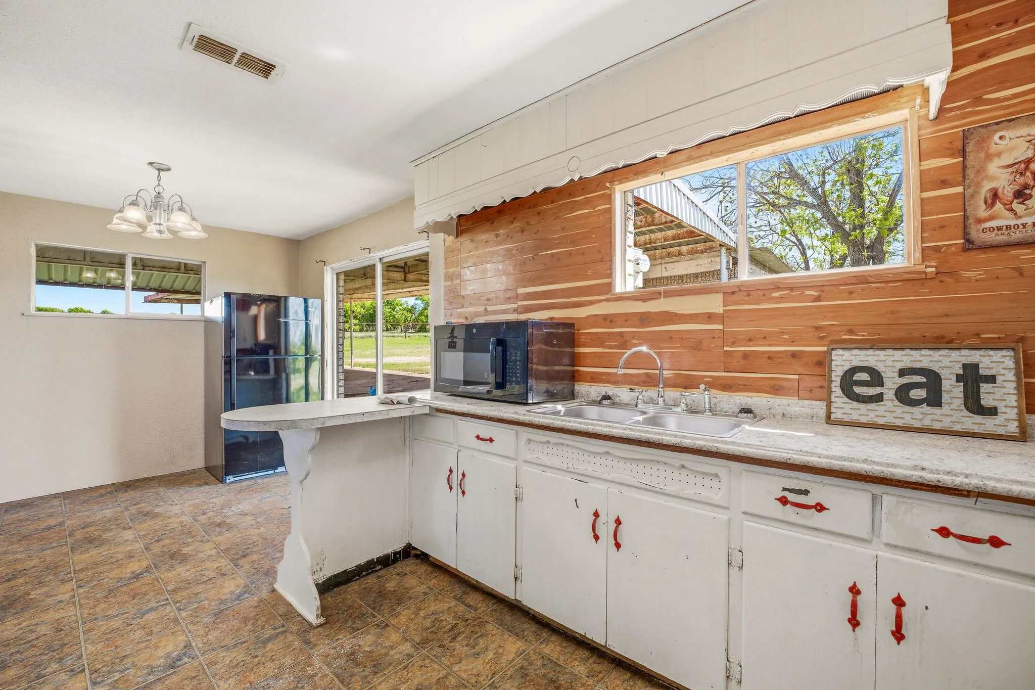 Kitchen with light countertops, black appliances, white cabinets, hanging lights, and wood walls