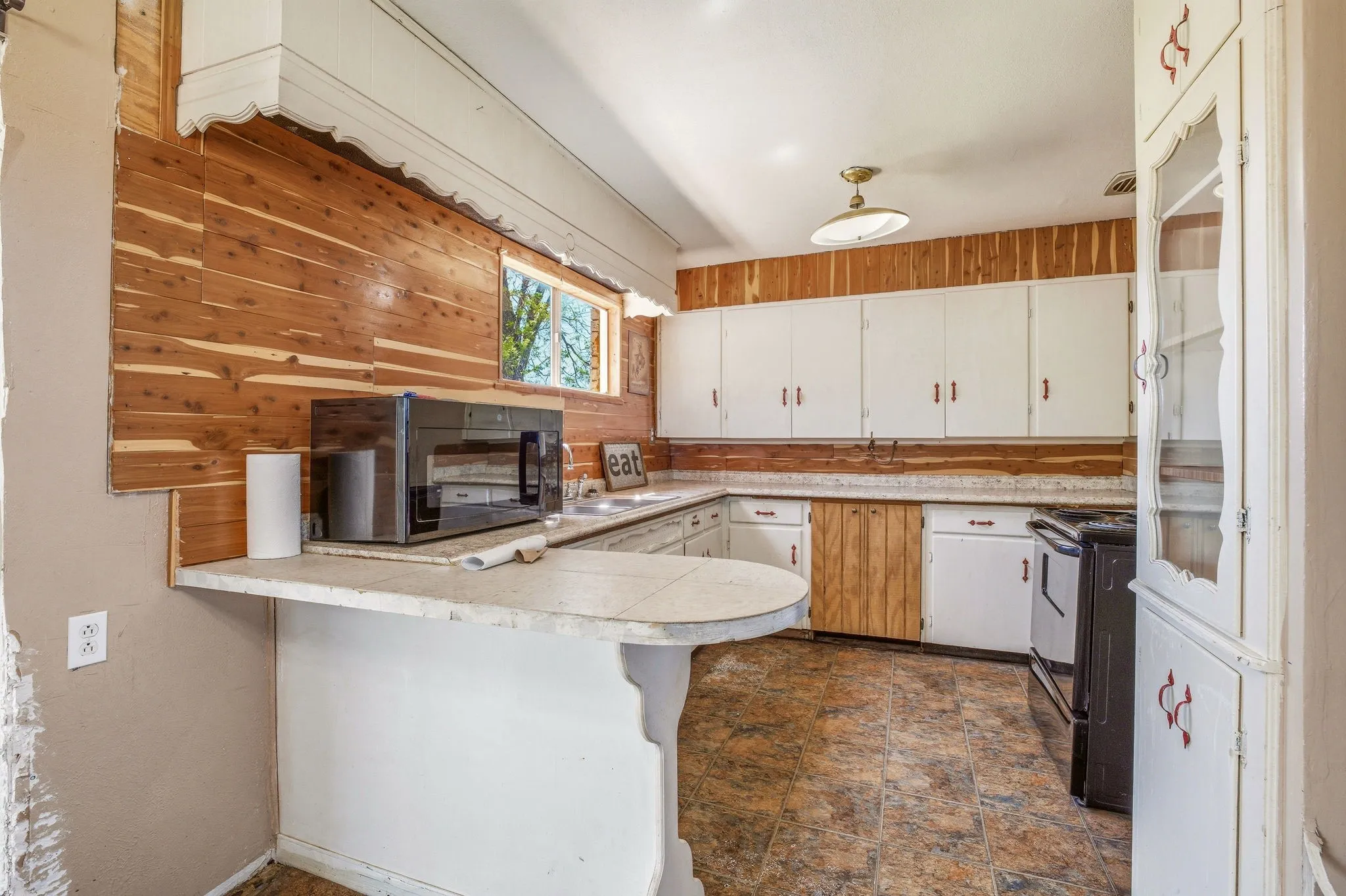 Kitchen featuring light countertops, white cabinetry, black appliances, stone finish flooring, and a peninsula