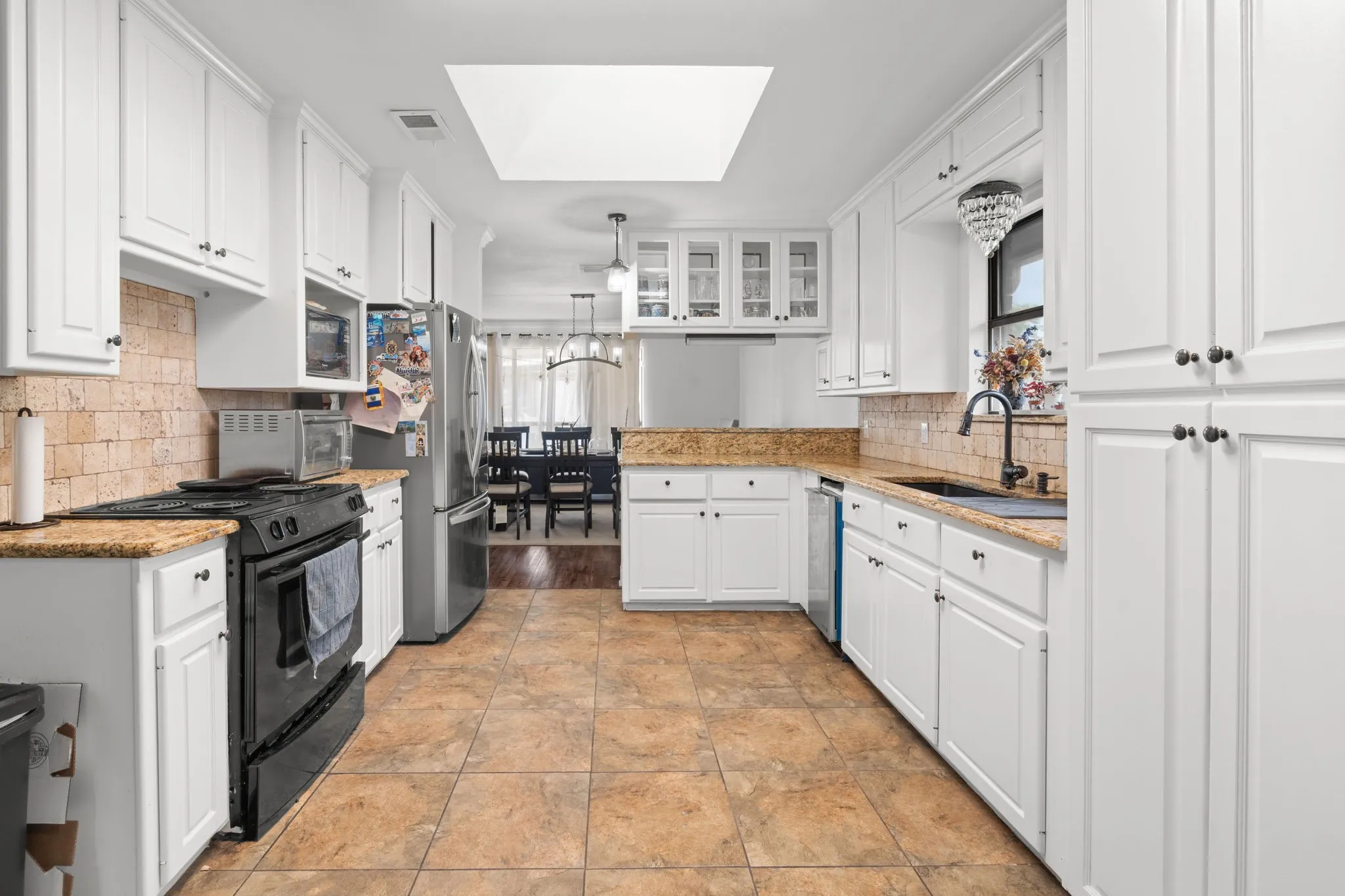 Kitchen featuring a skylight, white cabinets, stainless steel appliances, a peninsula, and light stone countertops