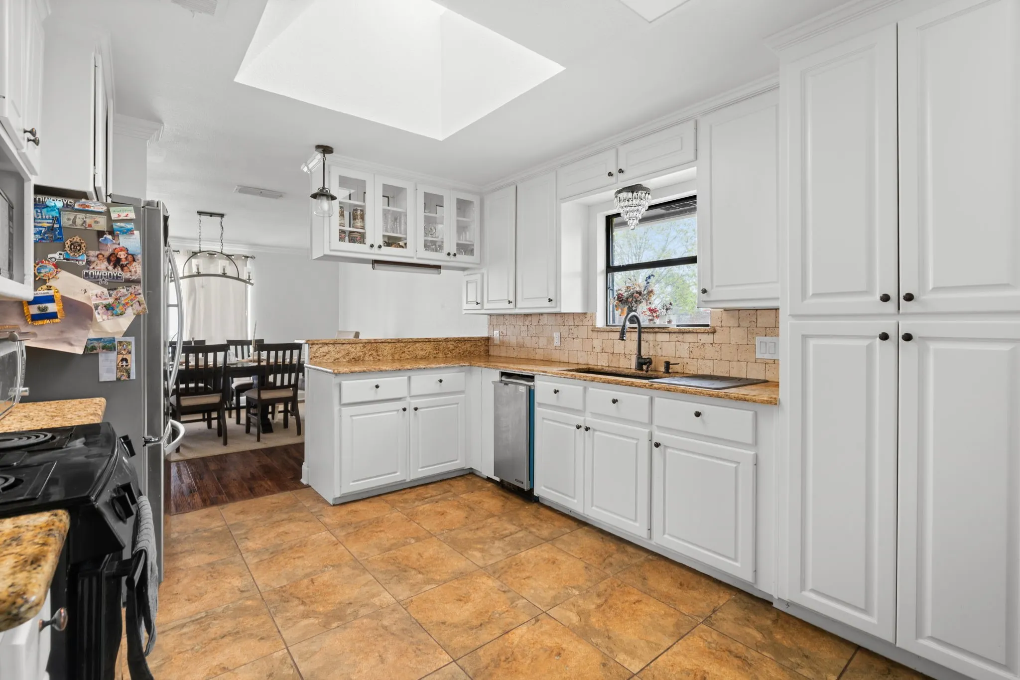 Kitchen with light stone counters, glass fronted cabinets, a peninsula, white cabinets, and tasteful backsplash