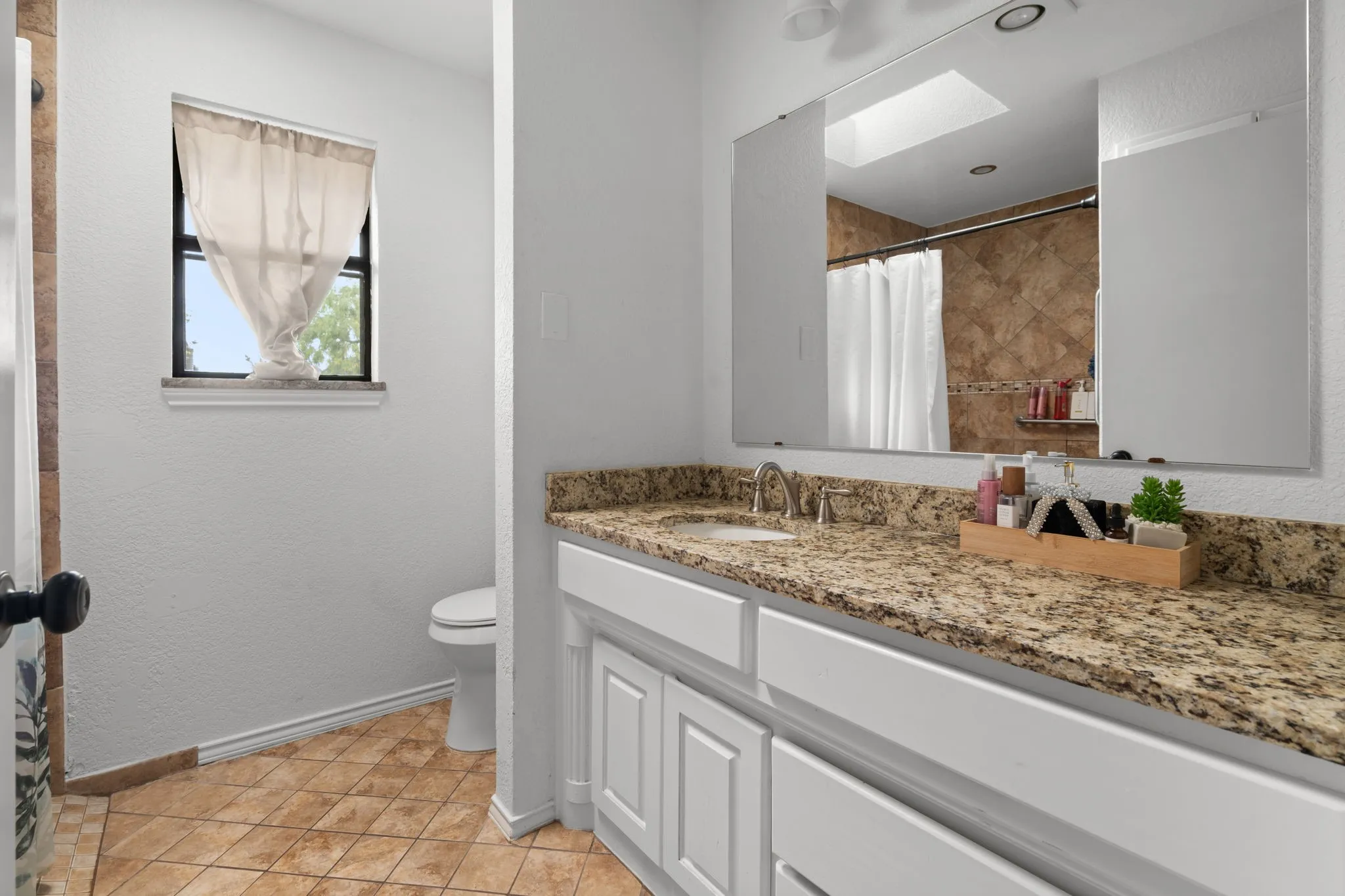 Bathroom featuring vanity, curtained shower, a skylight, and light tile patterned floors