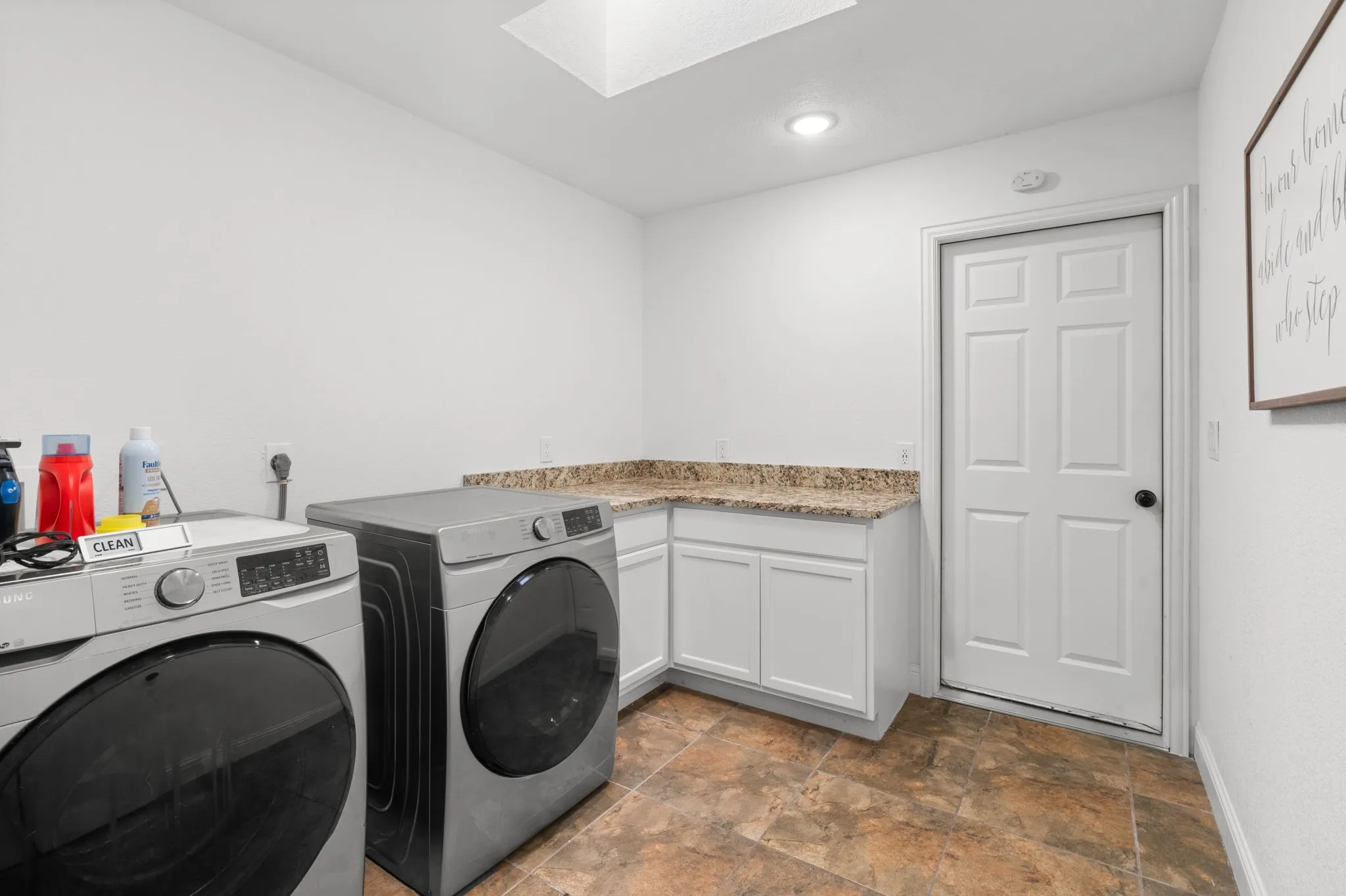 Laundry area with stone finish flooring, a skylight, washing machine and clothes dryer, and cabinet space