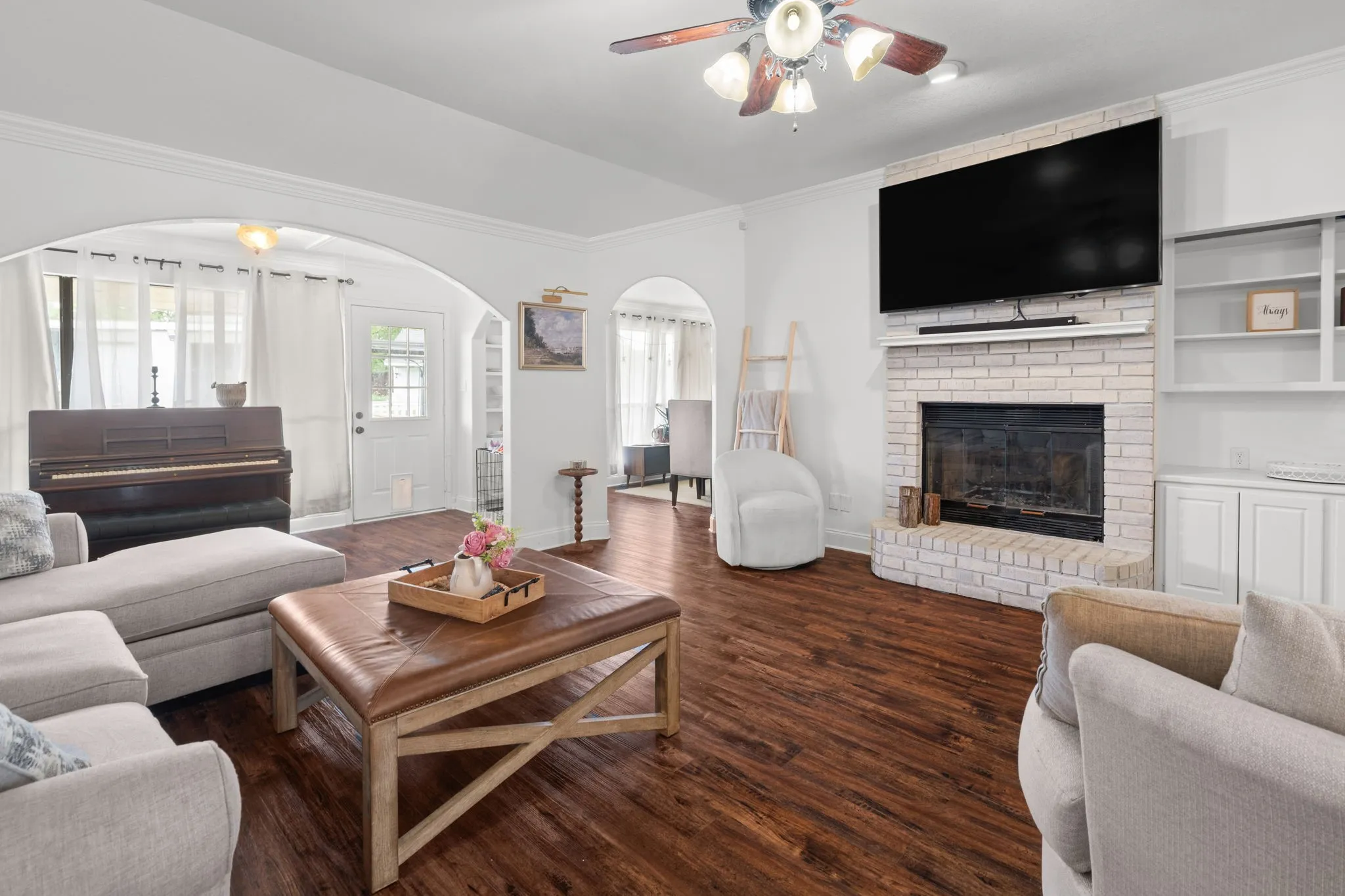 Living area with a ceiling fan, a fireplace, crown molding, dark wood-style flooring, and arched walkways