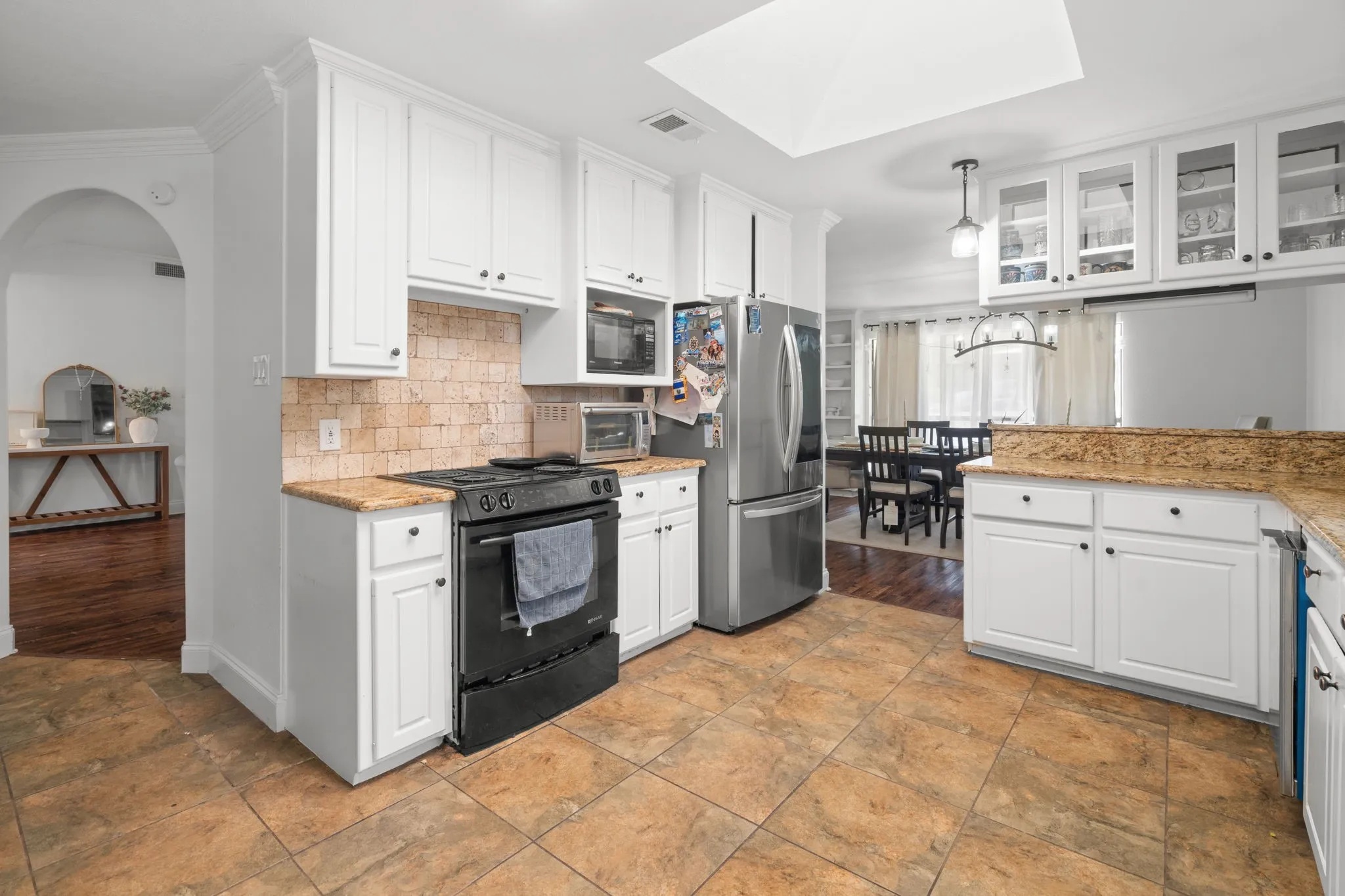 Kitchen featuring white cabinetry, black appliances, light stone counters, glass fronted cabinets, and a skylight