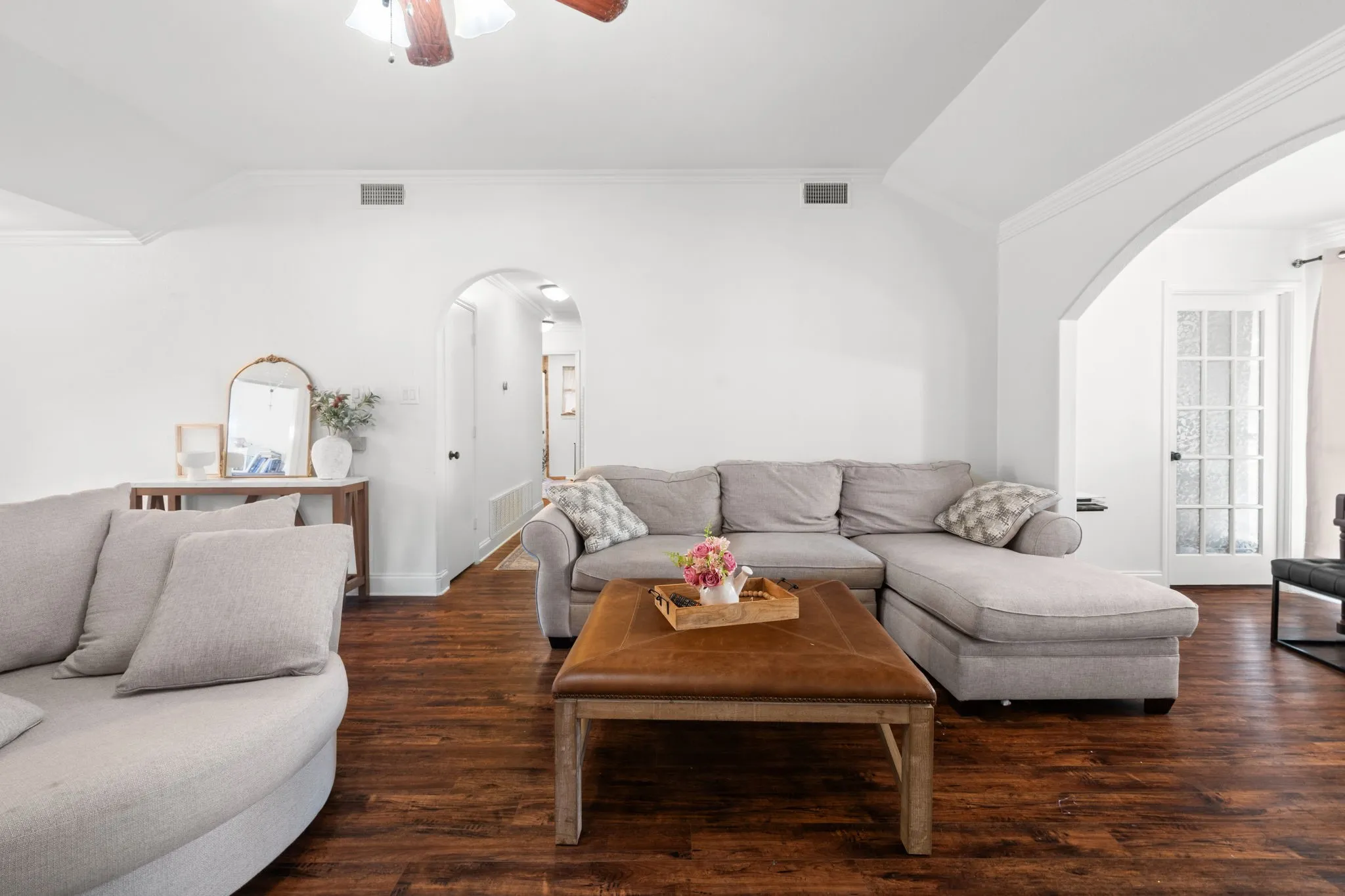 Living area featuring arched walkways, vaulted ceiling, ornamental molding, ceiling fan, and dark wood finished floors