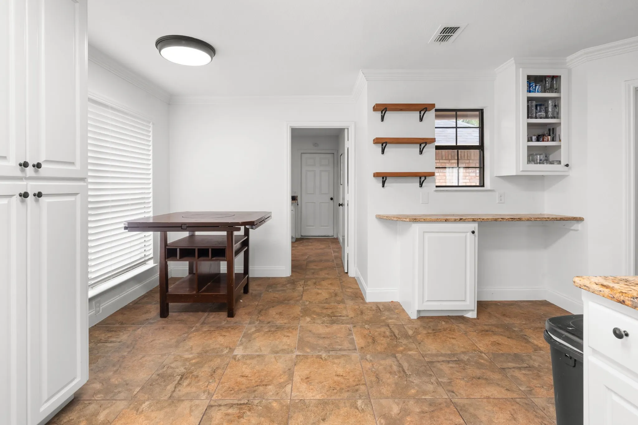 Kitchen with white cabinets, open shelves, crown molding, light stone countertops, and stone finish flooring