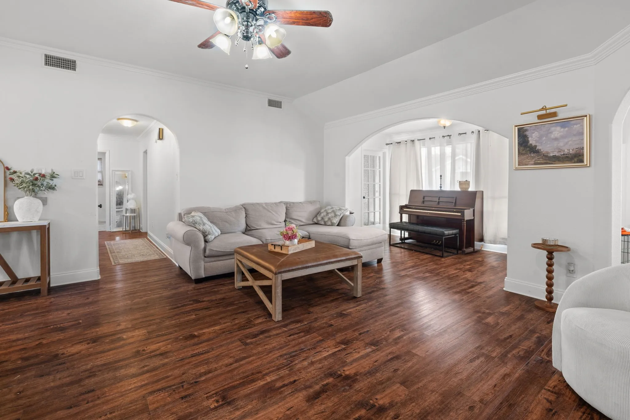 Living room featuring vaulted ceiling, arched walkways, a ceiling fan, dark wood-type flooring, and ornamental molding