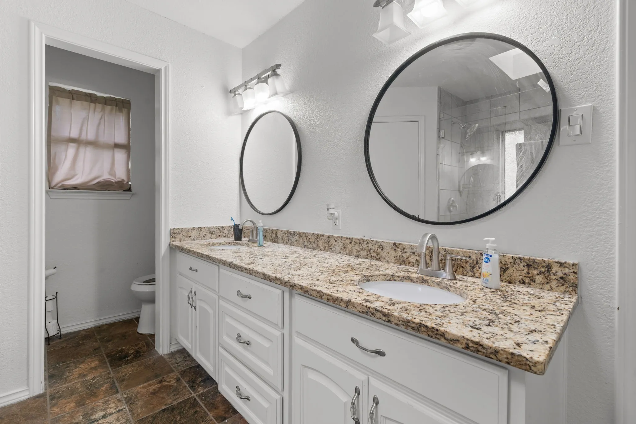 Bathroom with double vanity, a textured wall, and stone finish floors