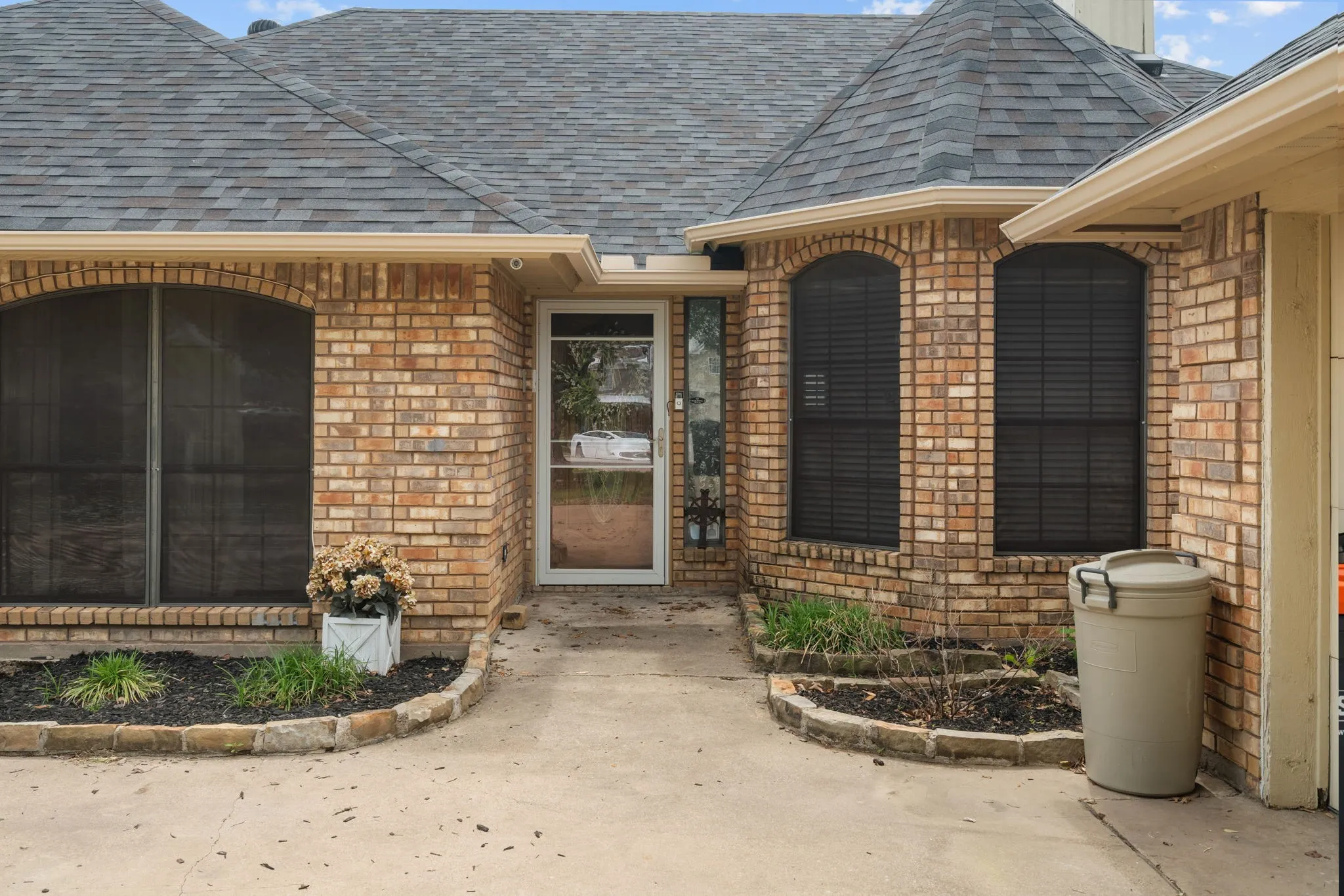 View of exterior entry with a shingled roof and brick siding