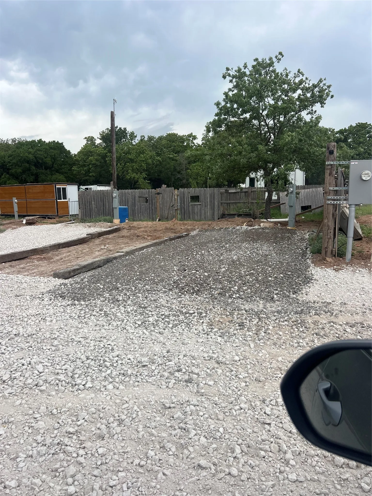 The property features a gravel lot with a wooden fence and mature trees in the background