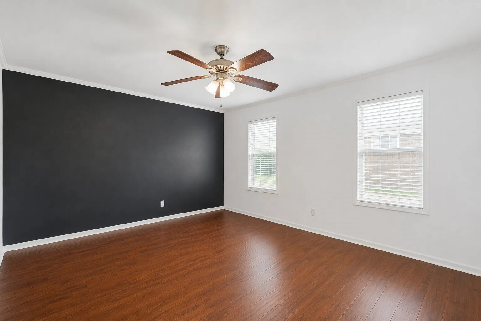 Spacious room featuring wood-finish flooring, a dark accent wall, white trim, and two windows with blinds