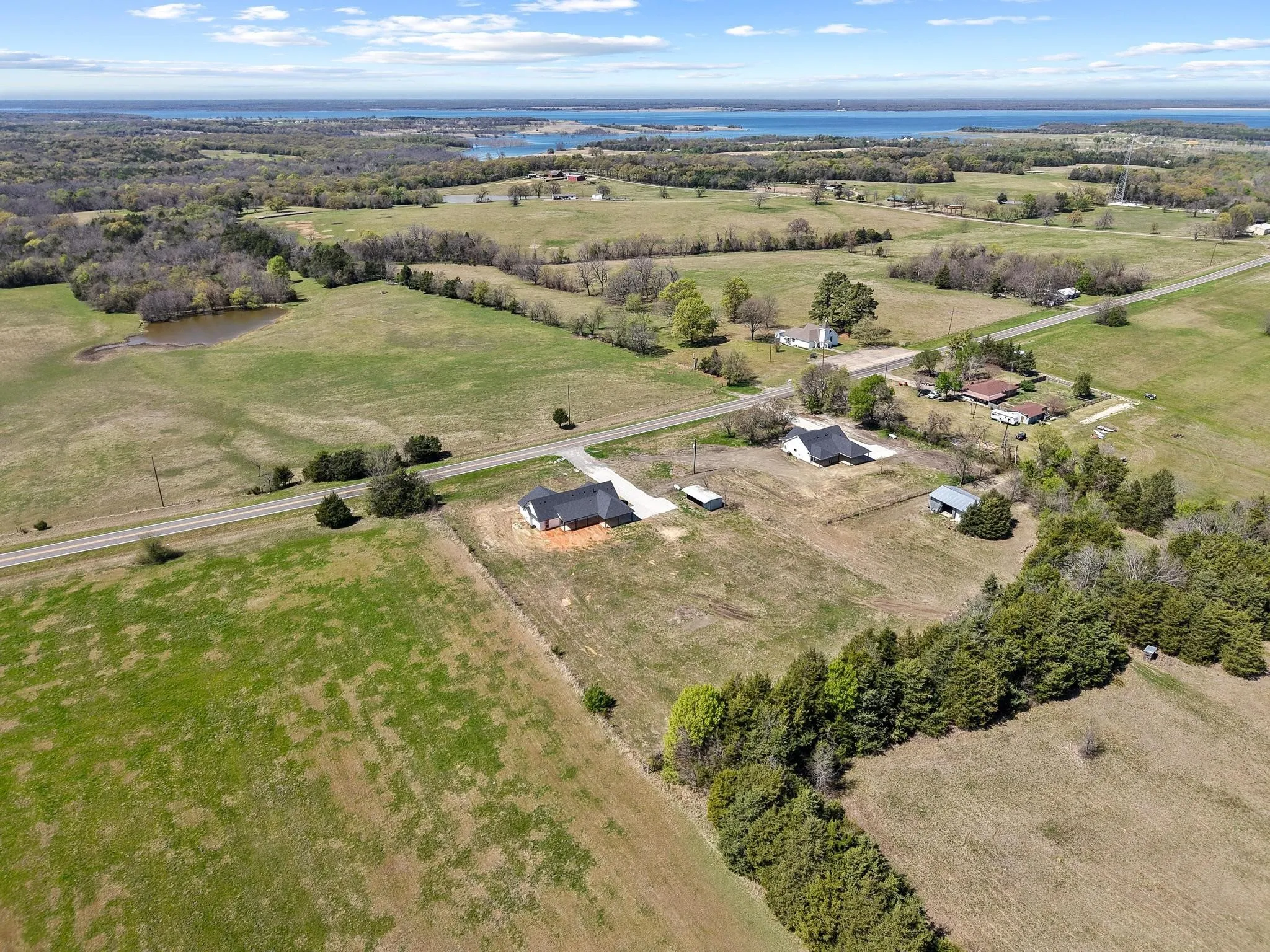 Aerial view showcasing the expansive grounds, featuring a large grassy area, wooded sections, and a visible body of water in the distance