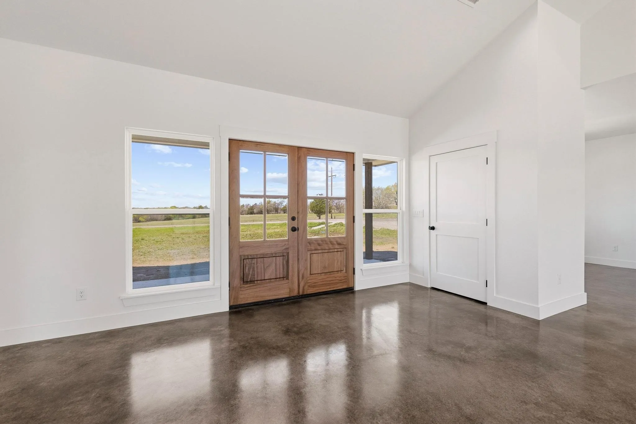 Welcoming entrance with rich wood double doors, polished concrete floors, and large windows offering views of the surrounding landscape
