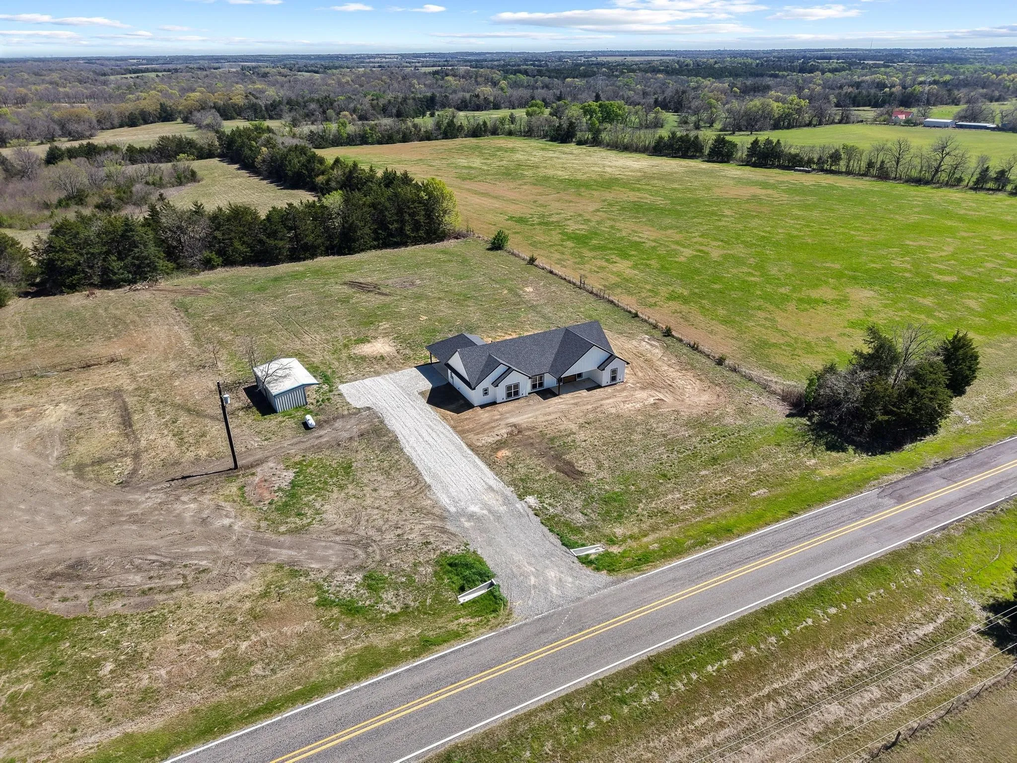 Aerial view of the property featuring a contemporary home with a dark roof, a gravel driveway, and a detached outbuilding