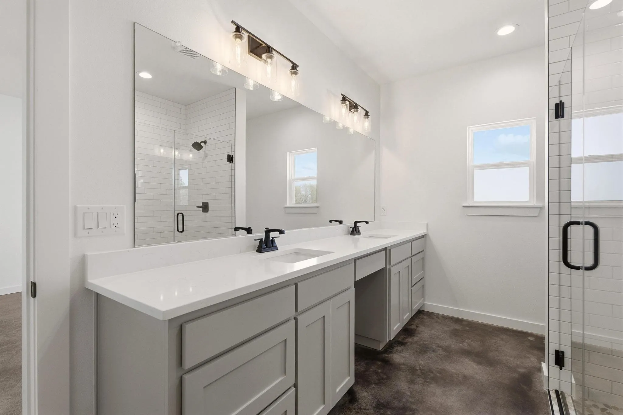 Bathroom with a dual vanity featuring light gray cabinetry and white countertops, a large mirror, and a glass-enclosed shower with subway tile