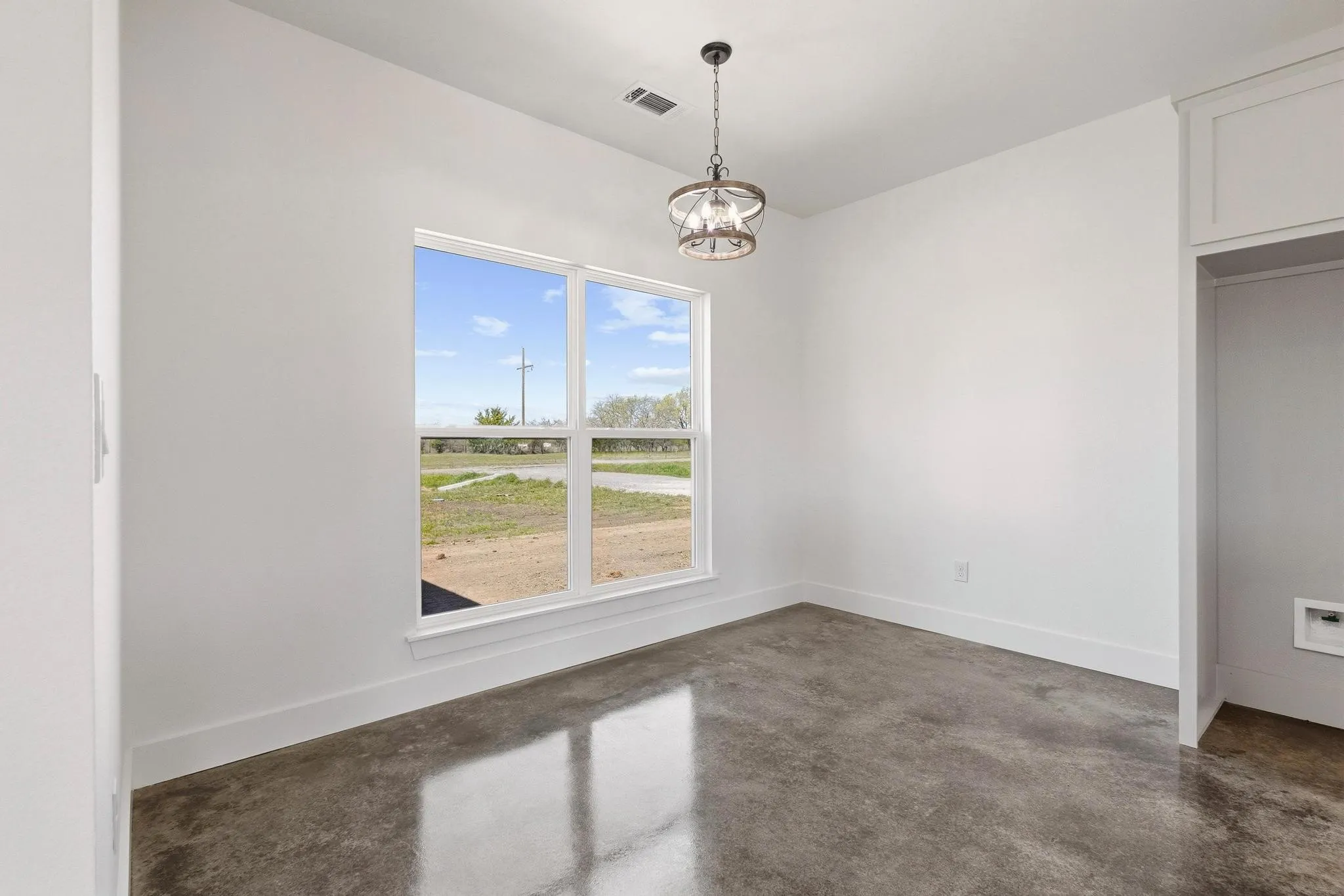 This room features a large window providing natural light, polished concrete flooring, white walls, and a contemporary ceiling light fixture
