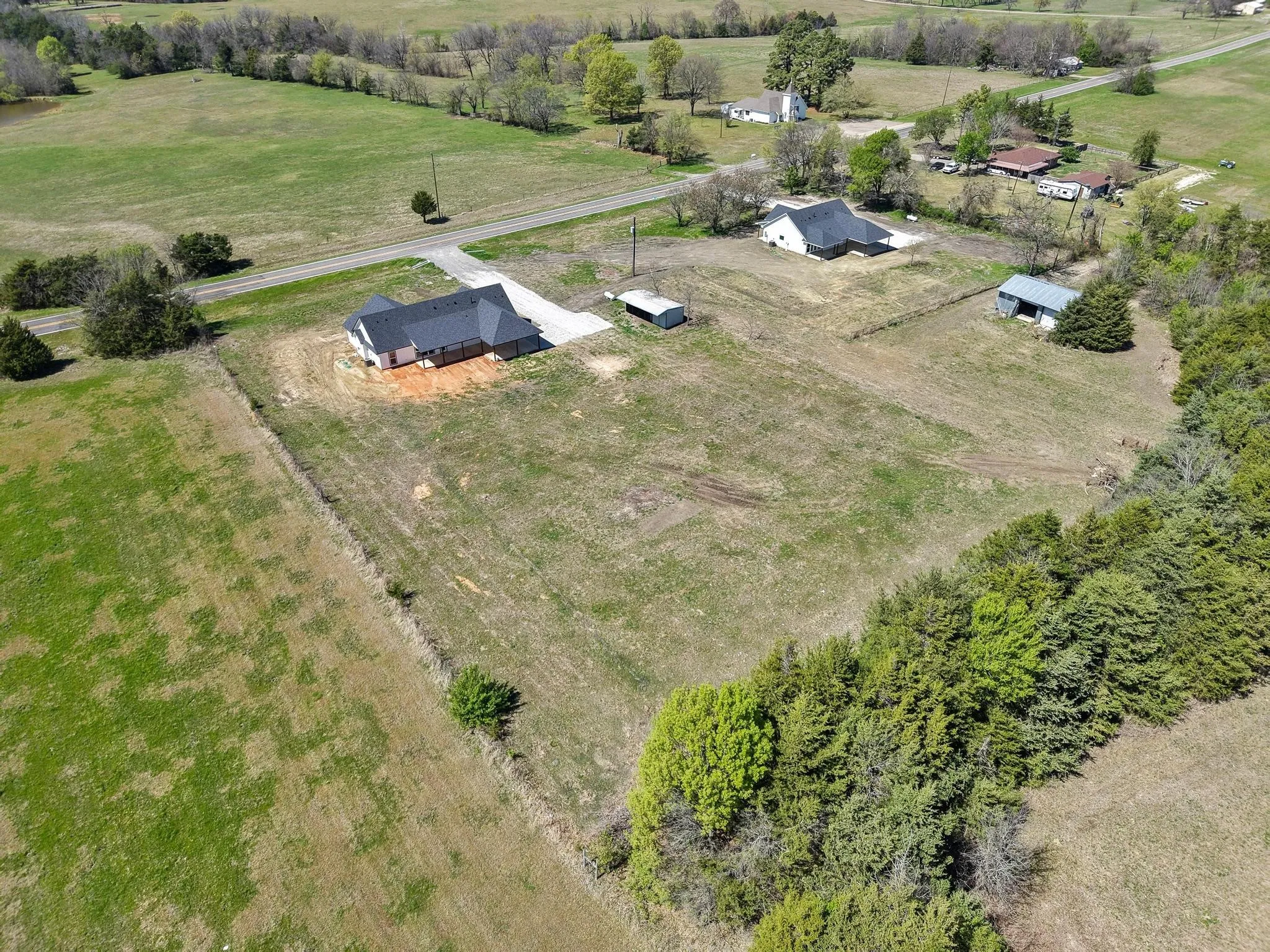This property features a single-story home with a dark roof, a driveway, and a separate outbuilding