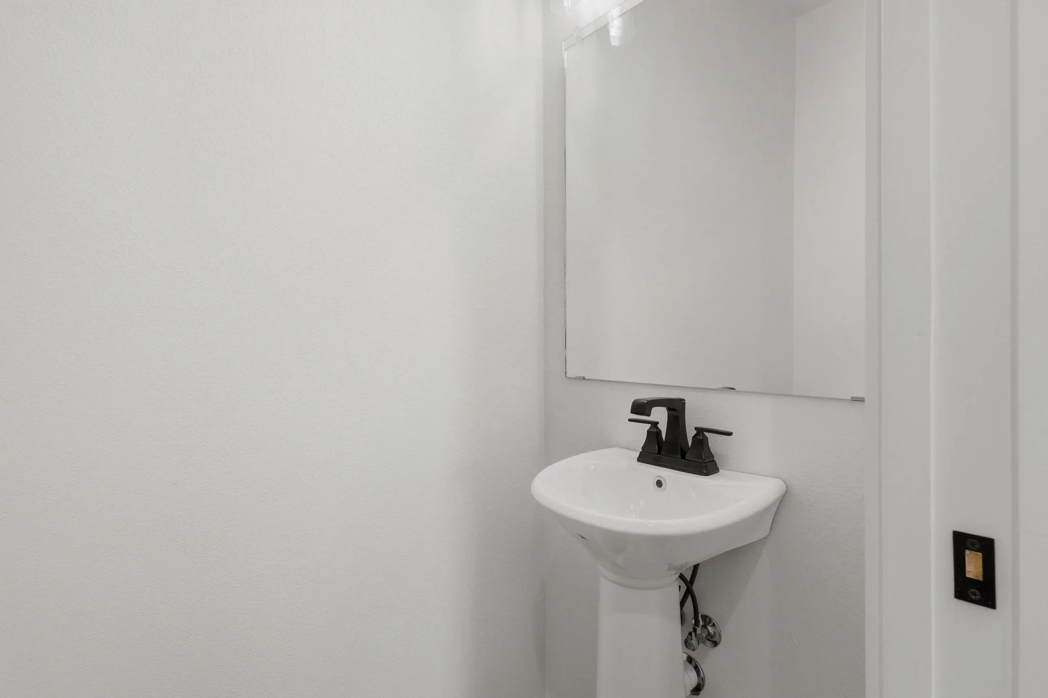 Bathroom featuring a white pedestal sink with a matte black faucet, and a wall-mounted mirror