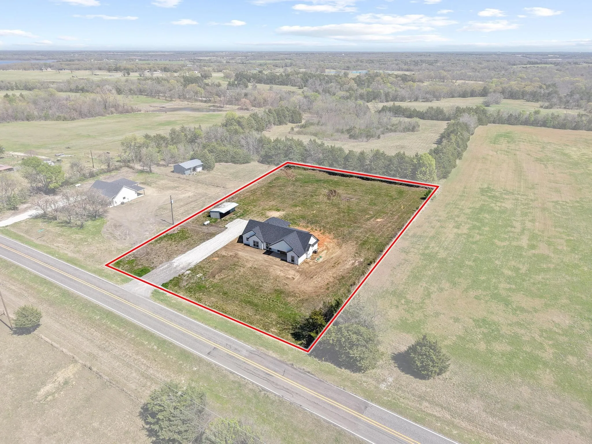 Aerial view of the property featuring a single-story home with a dark roof, a gravel driveway, and a covered carport