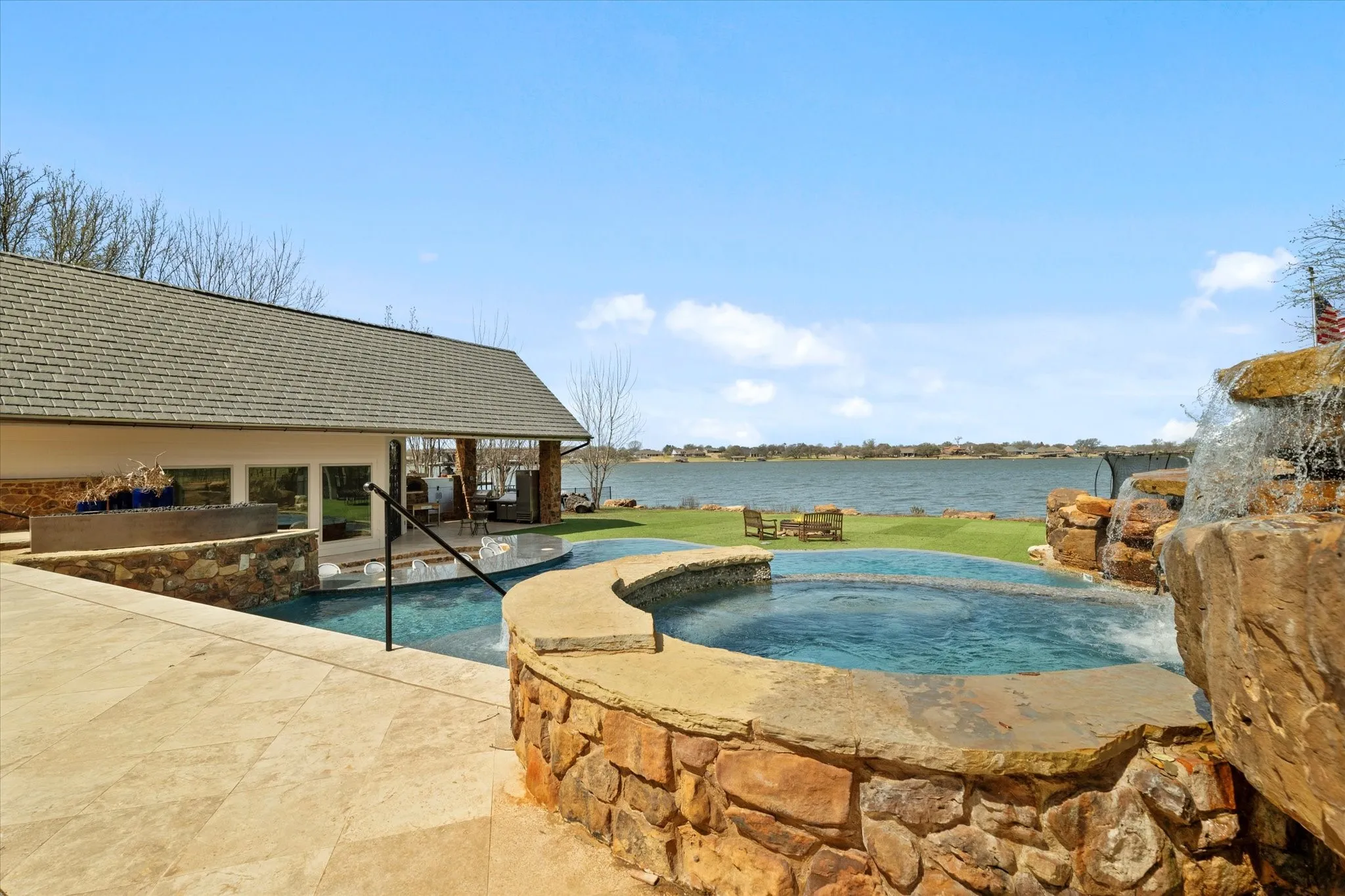 Outdoor living area featuring a stone-clad hot tub with a waterfall, a pool, and a paved patio area