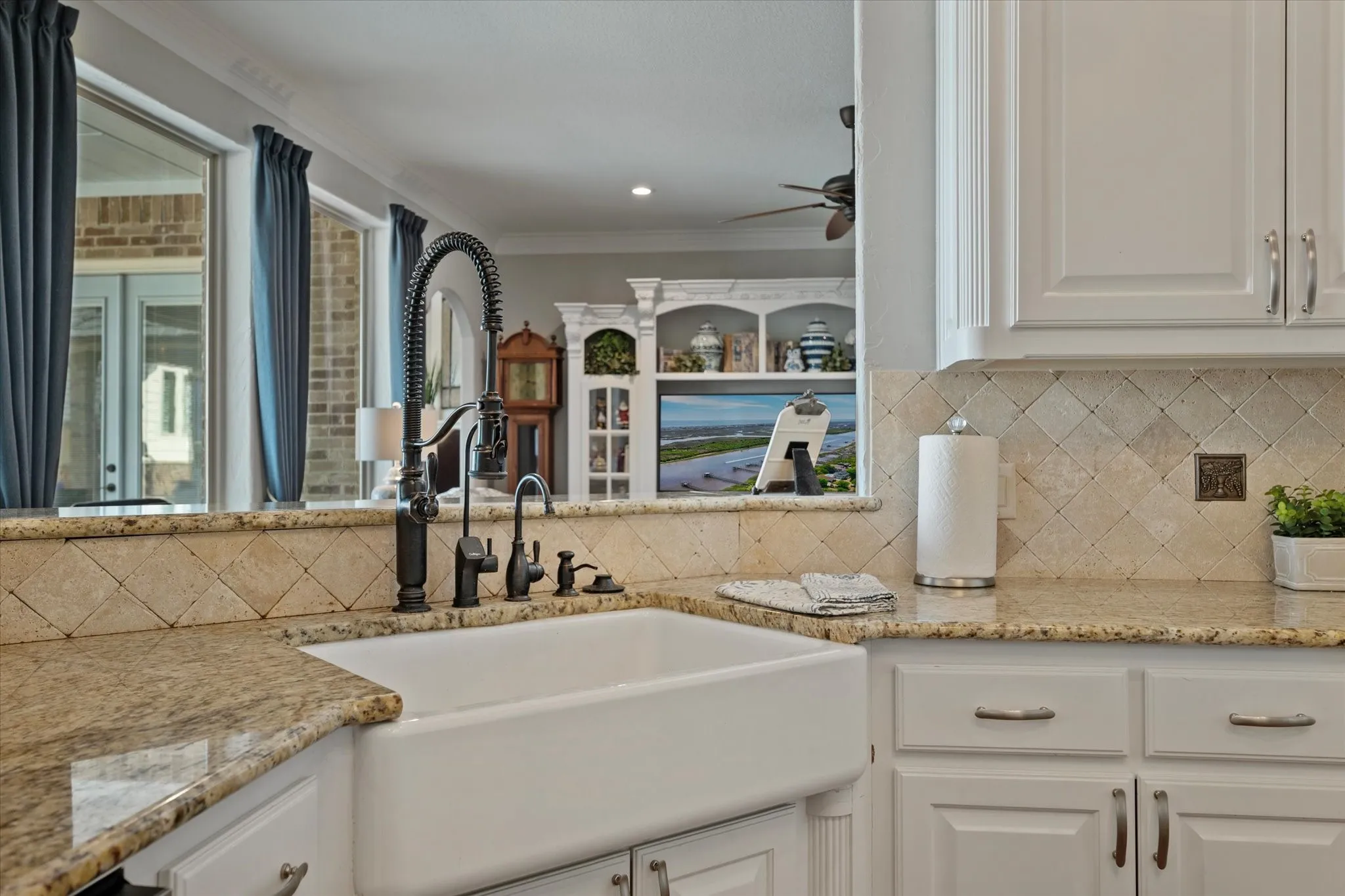 The kitchen features a white farmhouse sink with a dark-toned faucet, light-colored granite countertops, and a diagonally laid tile backsplash
