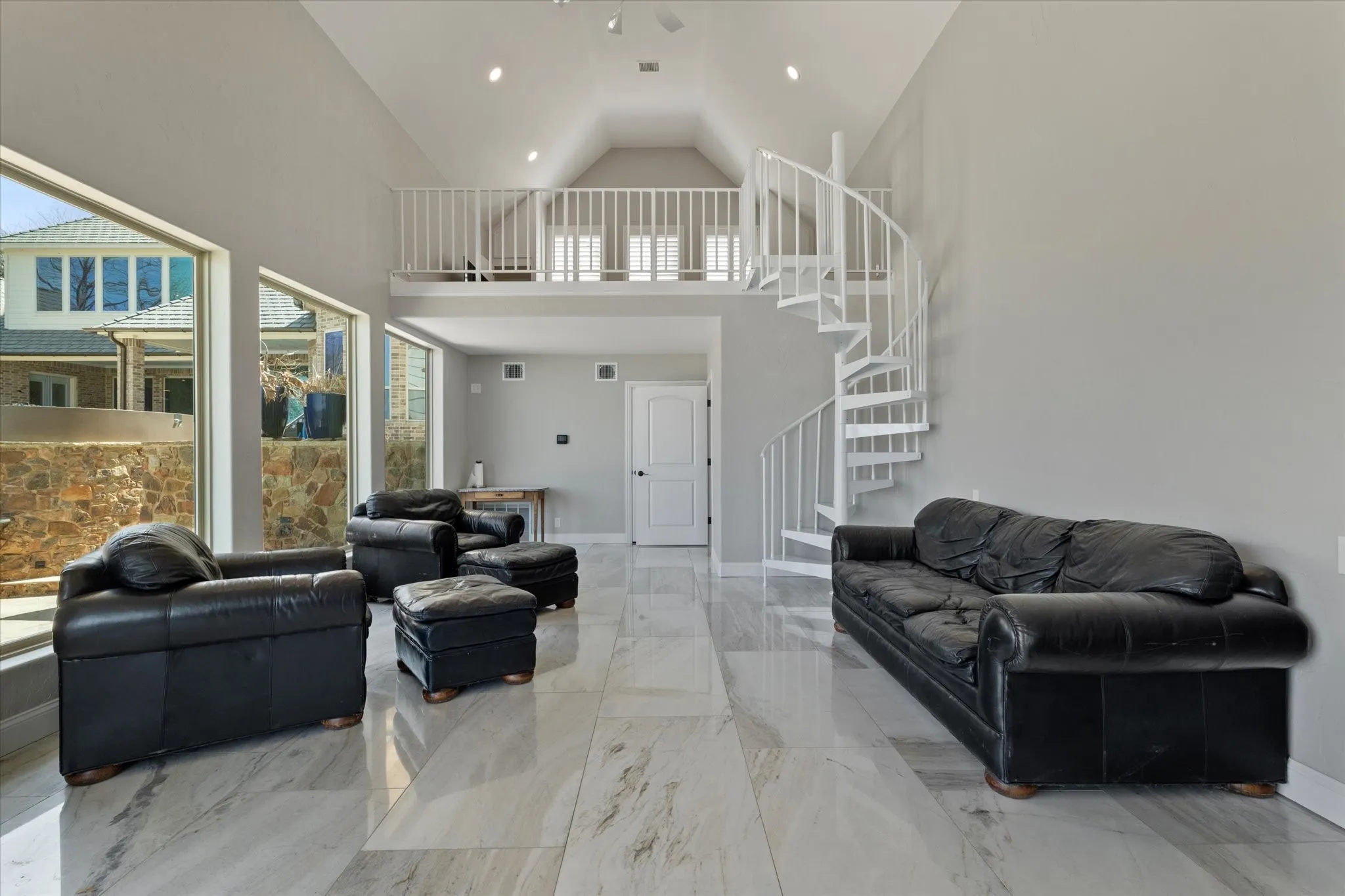 A spacious living area featuring high vaulted ceilings, large windows, and light-colored flooring