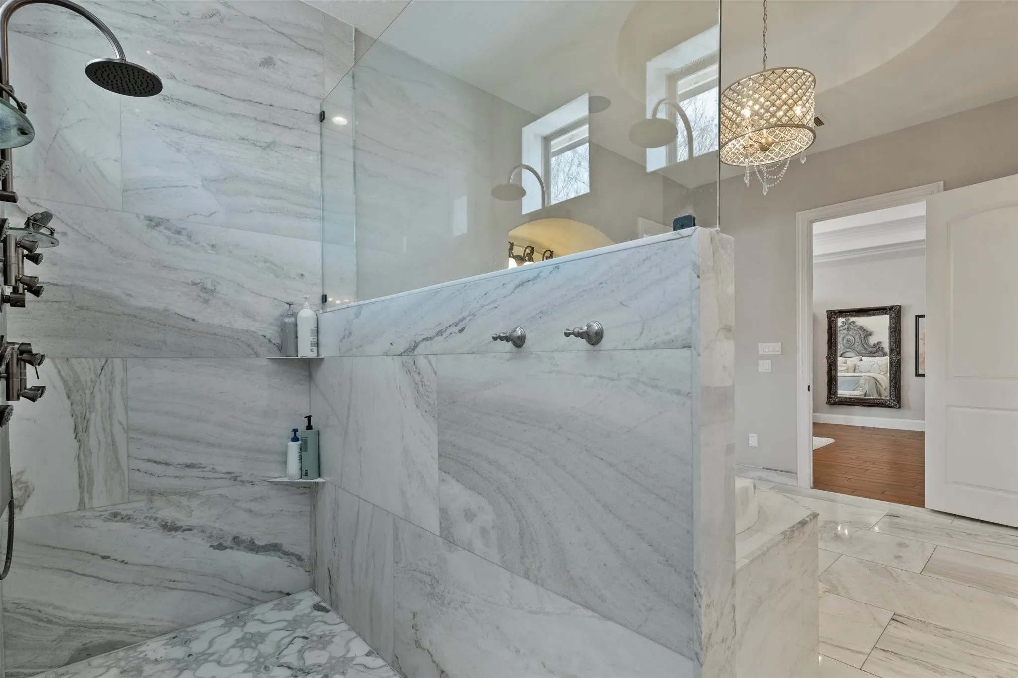 Luxurious shower with a rain shower head, multiple shower jets, and a built-in bench, all featuring expansive marble-patterned tiling