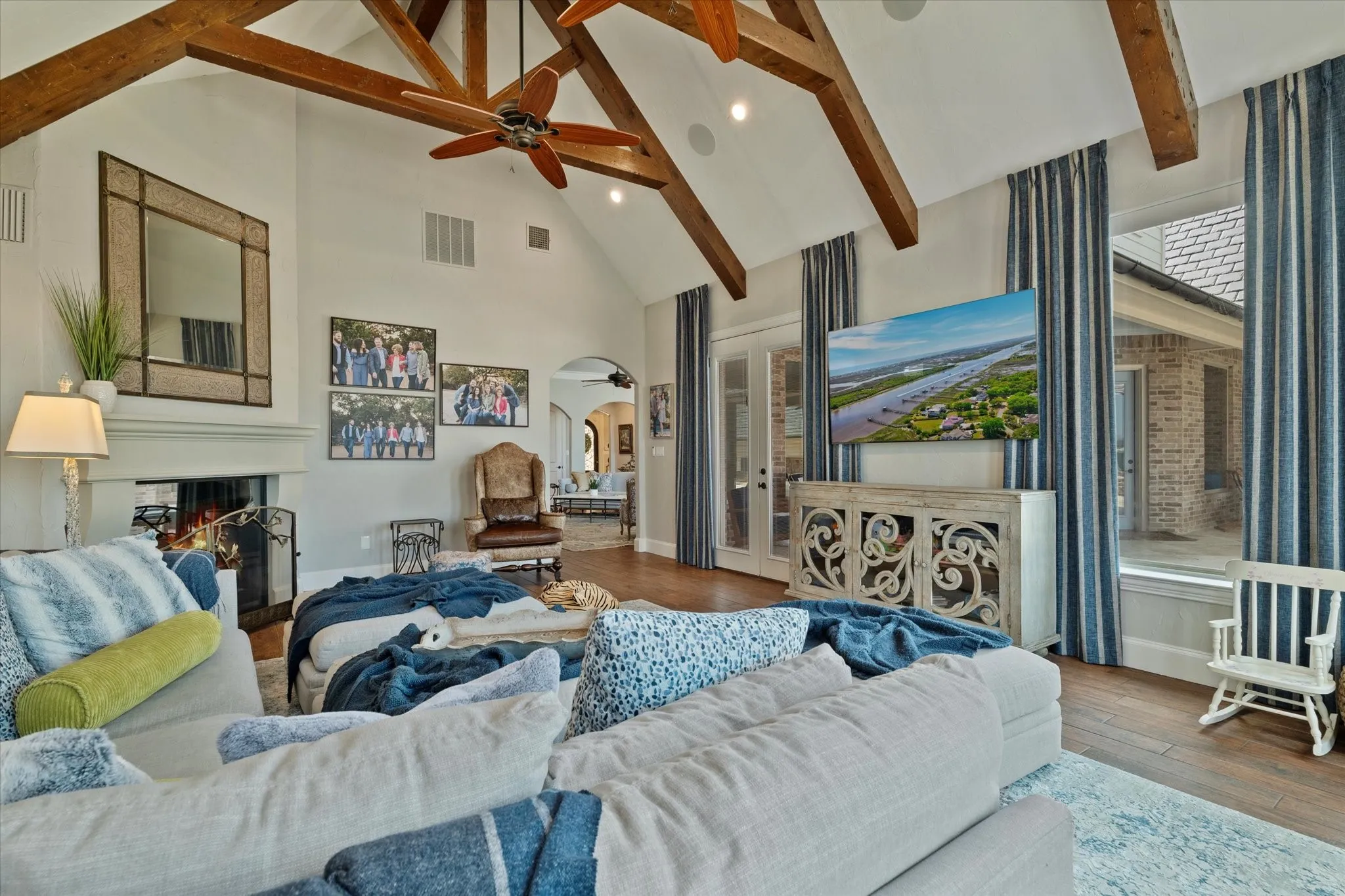 The living area features vaulted ceilings with exposed wood beams, a fireplace, and large windows with privacy drapes