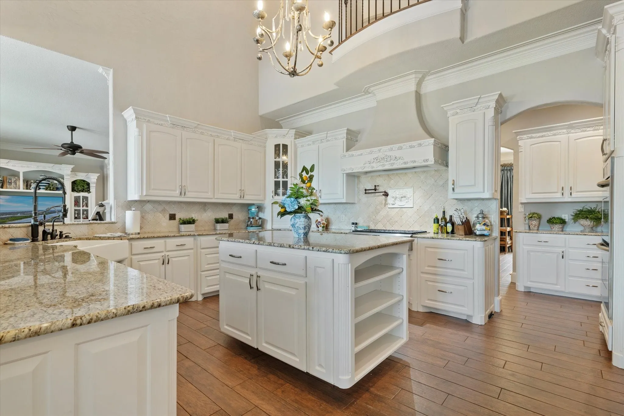 The kitchen features white cabinetry, granite countertops, a central island with storage, and rich hardwood flooring