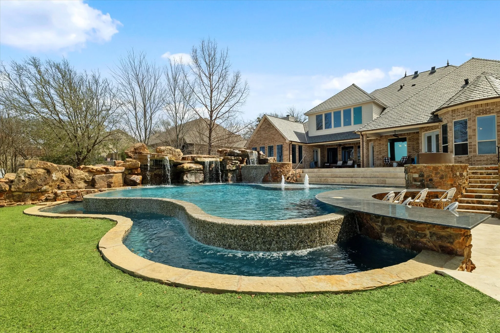 The property features an extensive backyard with a multi-level swimming pool, an integrated stone waterfall, and a built-in outdoor bar area