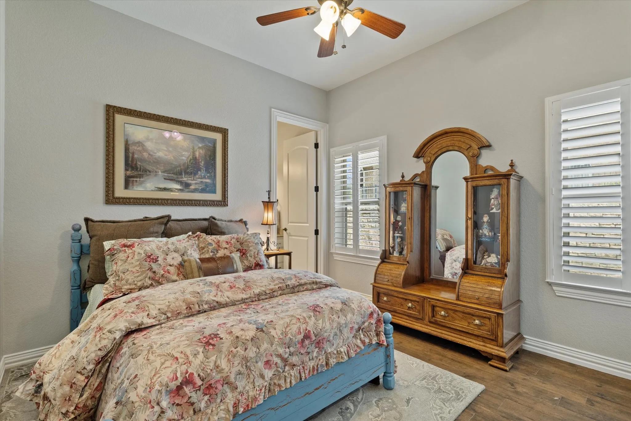 This room features wood flooring, two windows with white plantation shutters, and a ceiling fan with integrated lighting