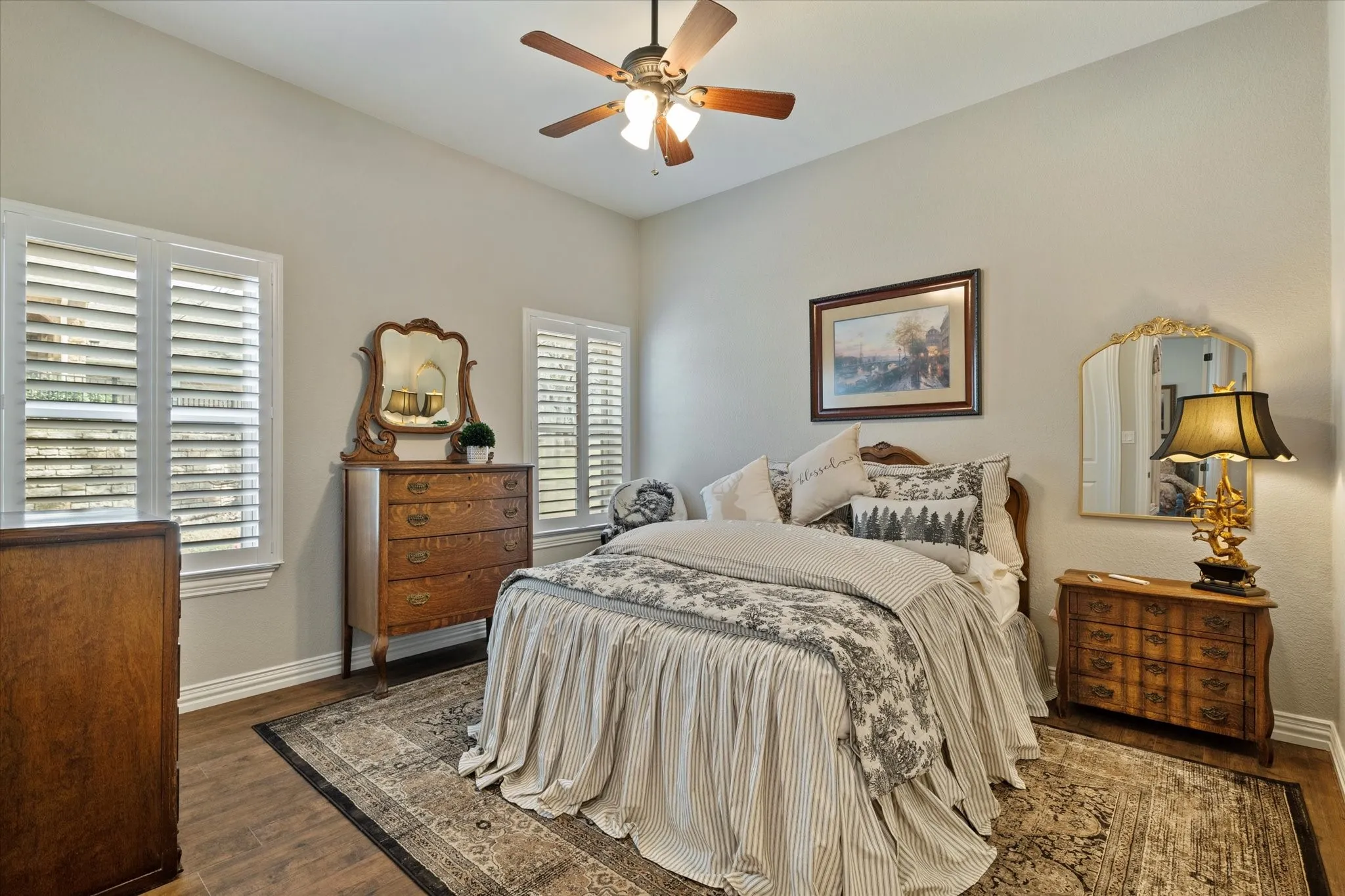 This room features hardwood style flooring, windows with louvered shutters, and a ceiling fan with integrated lighting