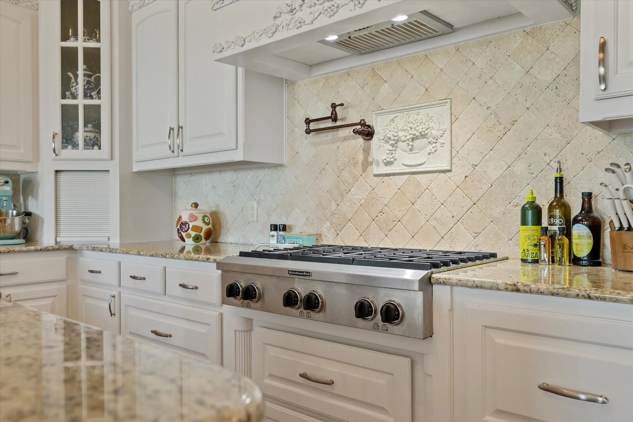 Kitchen featuring white cabinetry, granite countertops, a stainless steel gas range, and a tiled backsplash with decorative accents