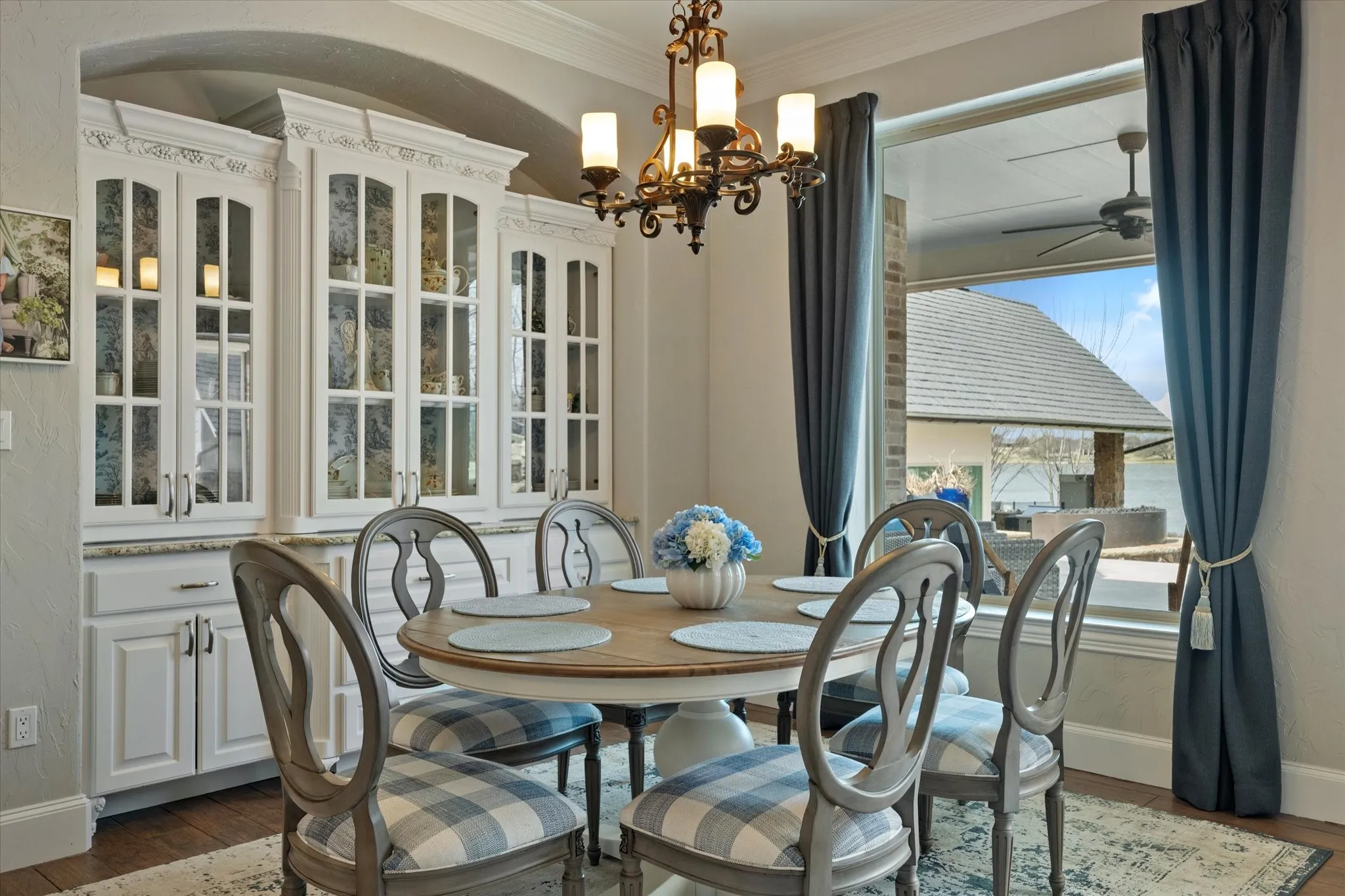 Dining area featuring white built-in cabinetry with glass panel doors, a large window, and an ornate chandelier