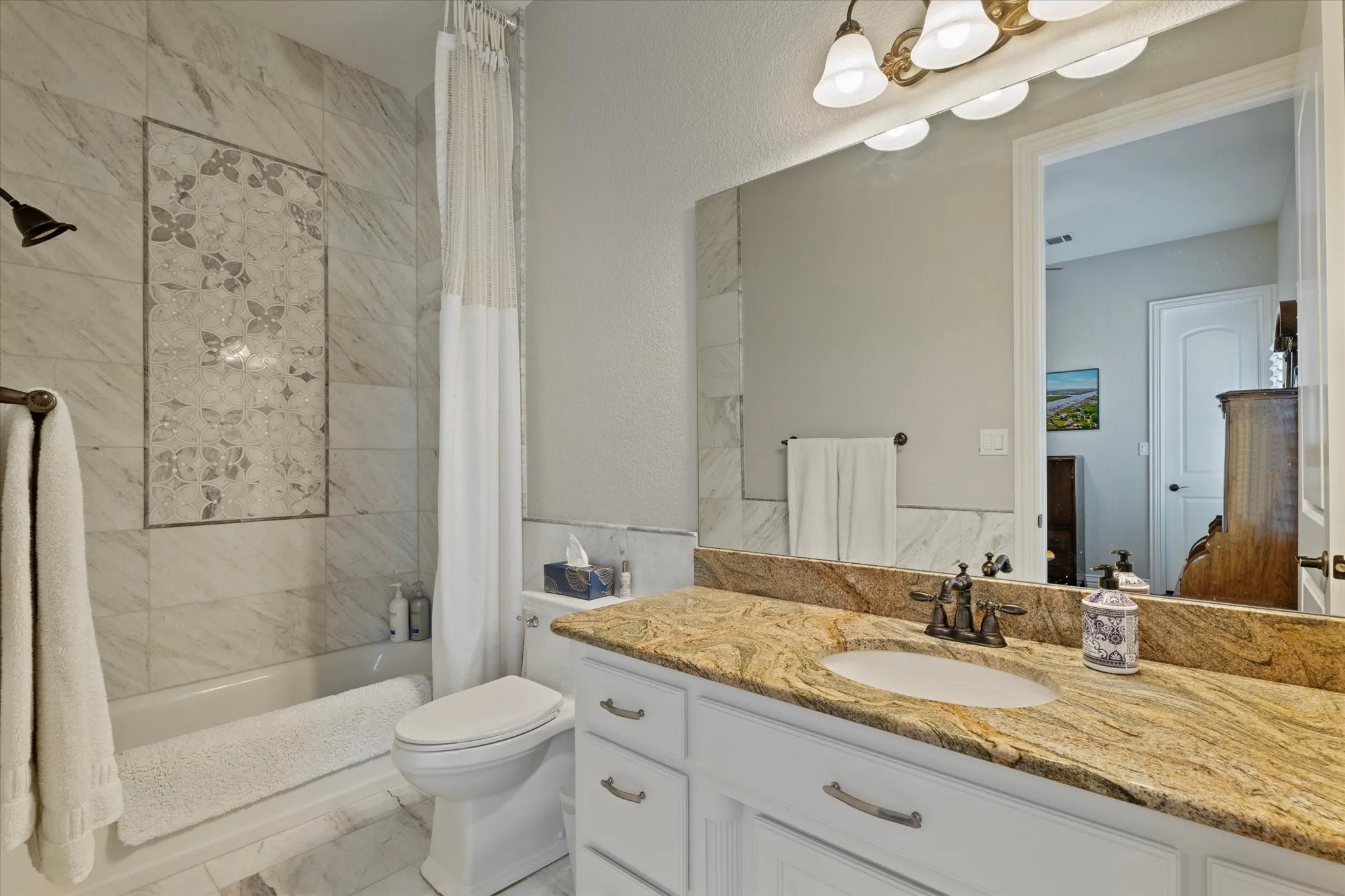 Bathroom featuring a granite countertop vanity with a single sink, a full-width mirror, and a bathtub with a tiled shower surround