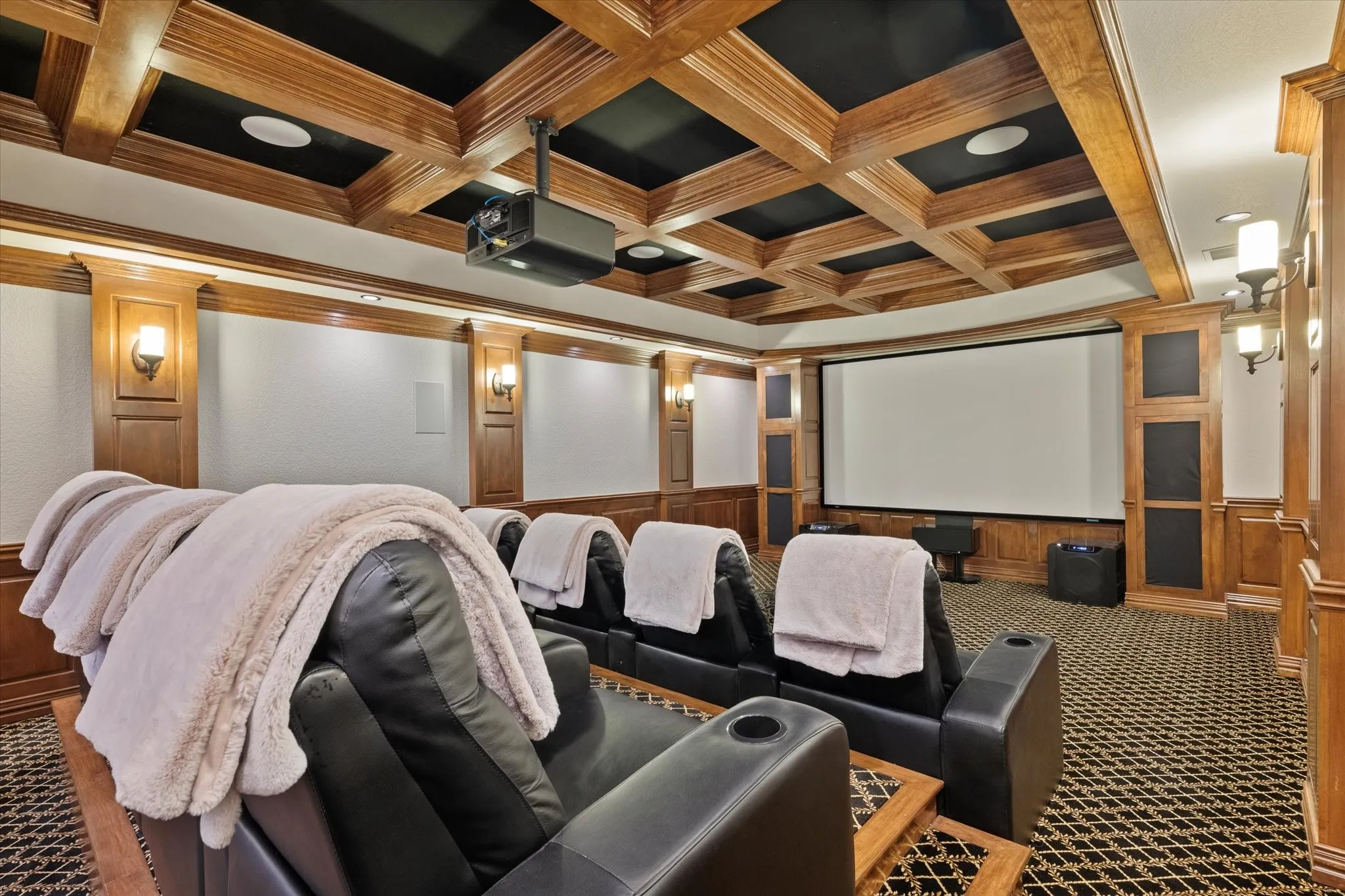 This dedicated entertainment area features a coffered wood ceiling, a large projection screen, and integrated wall sconces